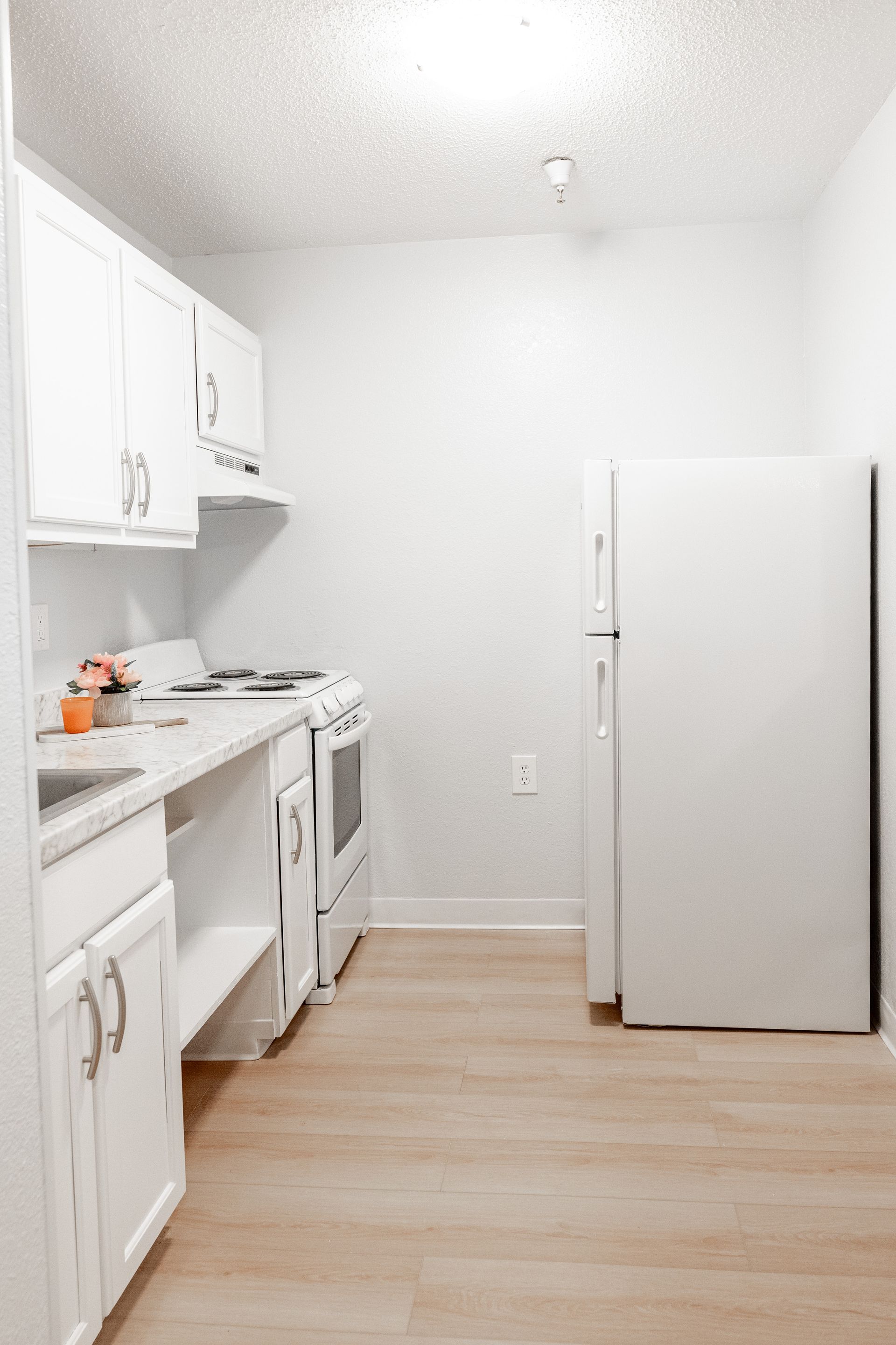 A kitchen with white cabinets , a refrigerator , a stove , and a sink.