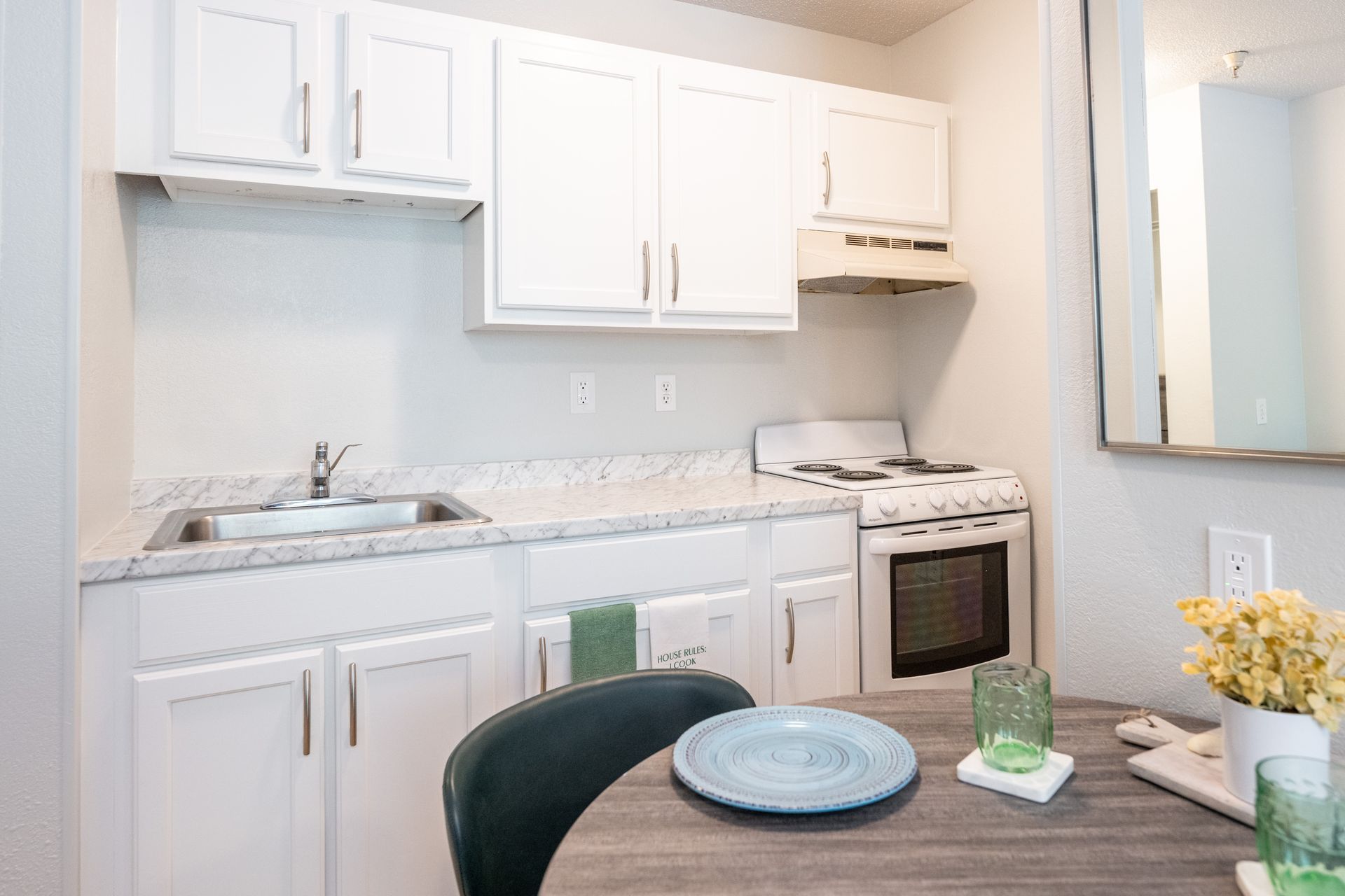 A kitchen with white cabinets , a stove , a sink , and a table.