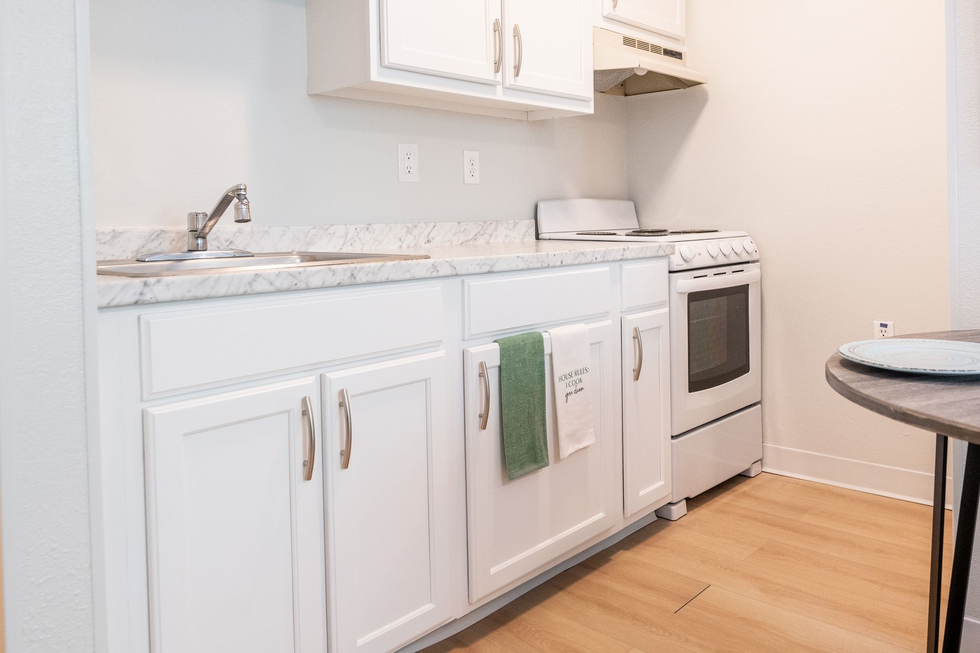 A kitchen with white cabinets , a stove , a sink , and a table.