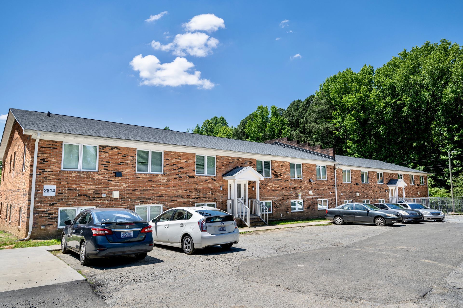 A row of cars are parked in front of a brick apartment building.