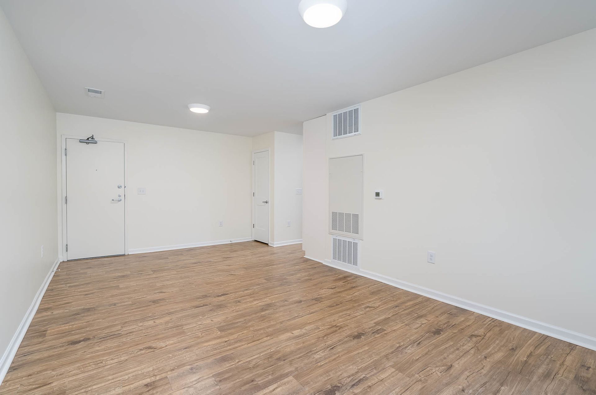 An empty living room with hardwood floors and white walls.