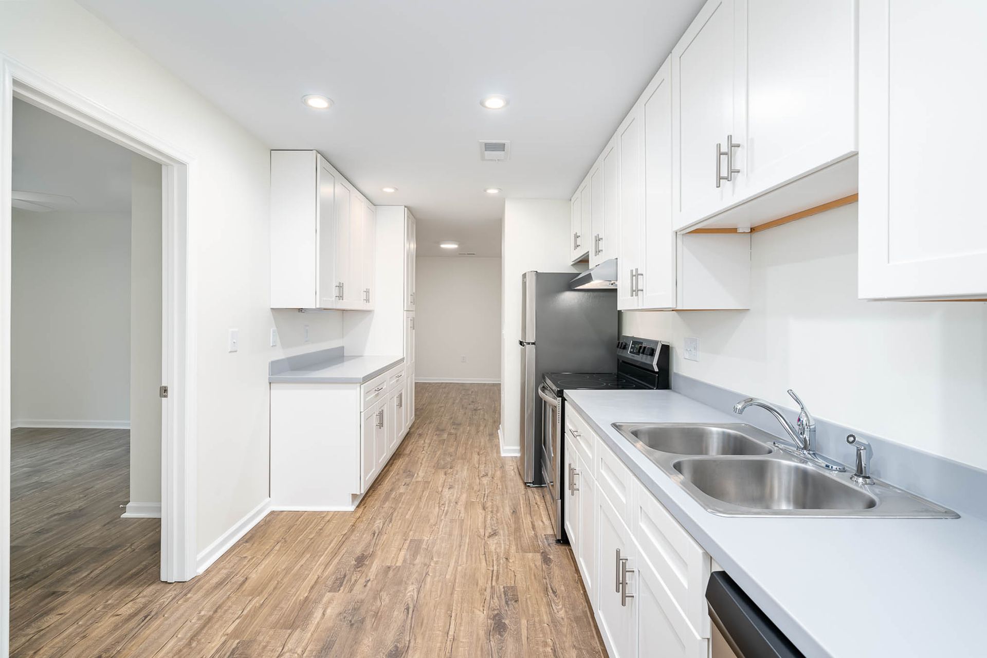 A kitchen with white cabinets , stainless steel appliances , a sink and a refrigerator.