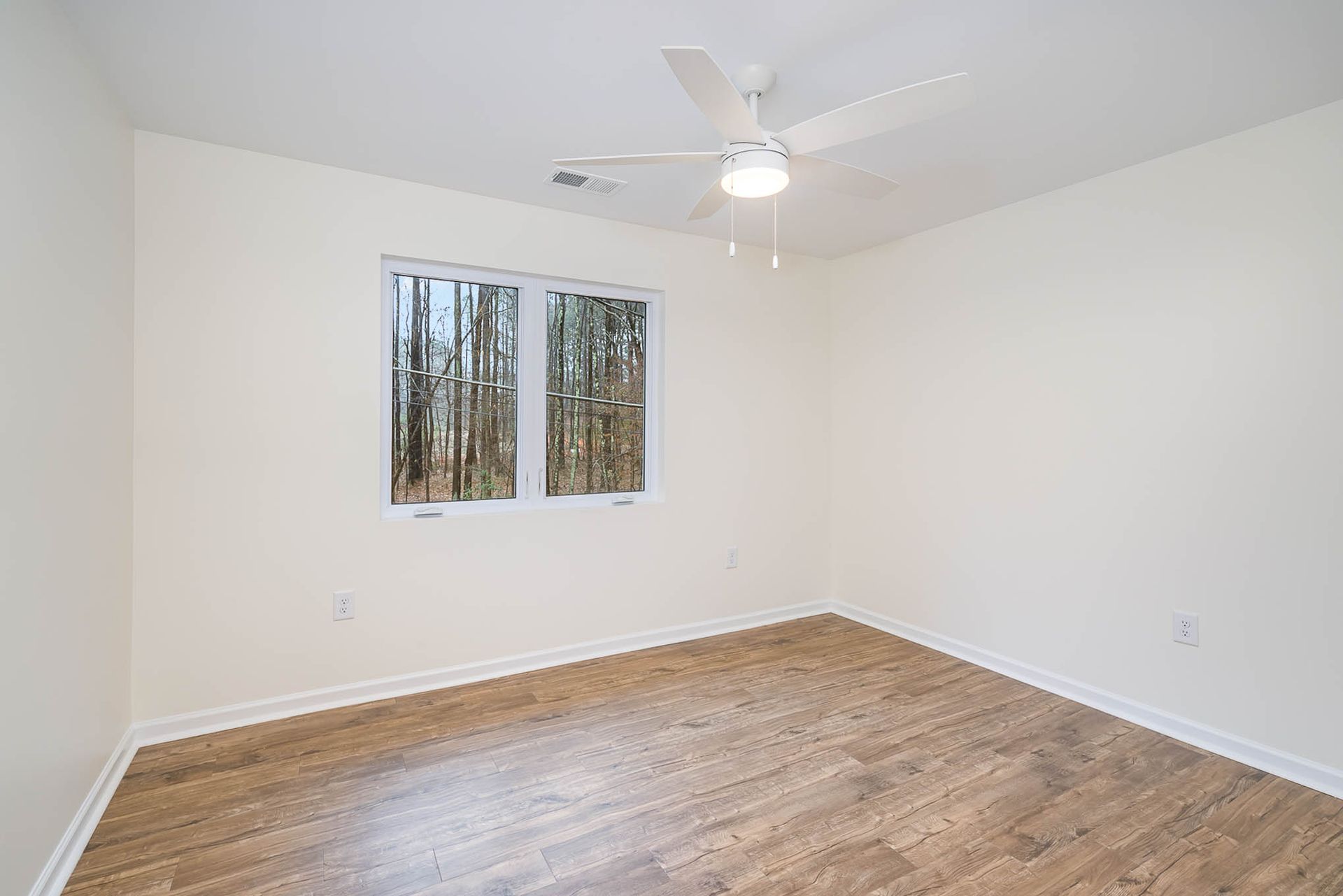 An empty bedroom with hardwood floors and a ceiling fan.