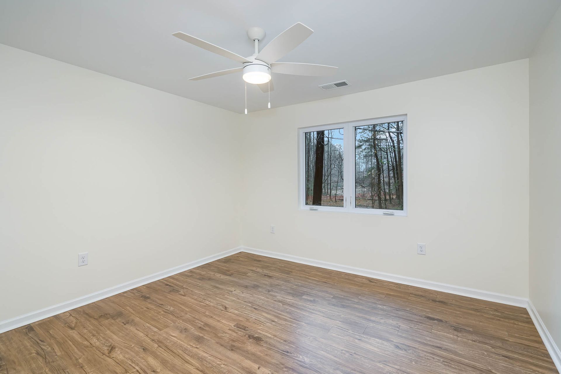 An empty bedroom with hardwood floors and a ceiling fan.