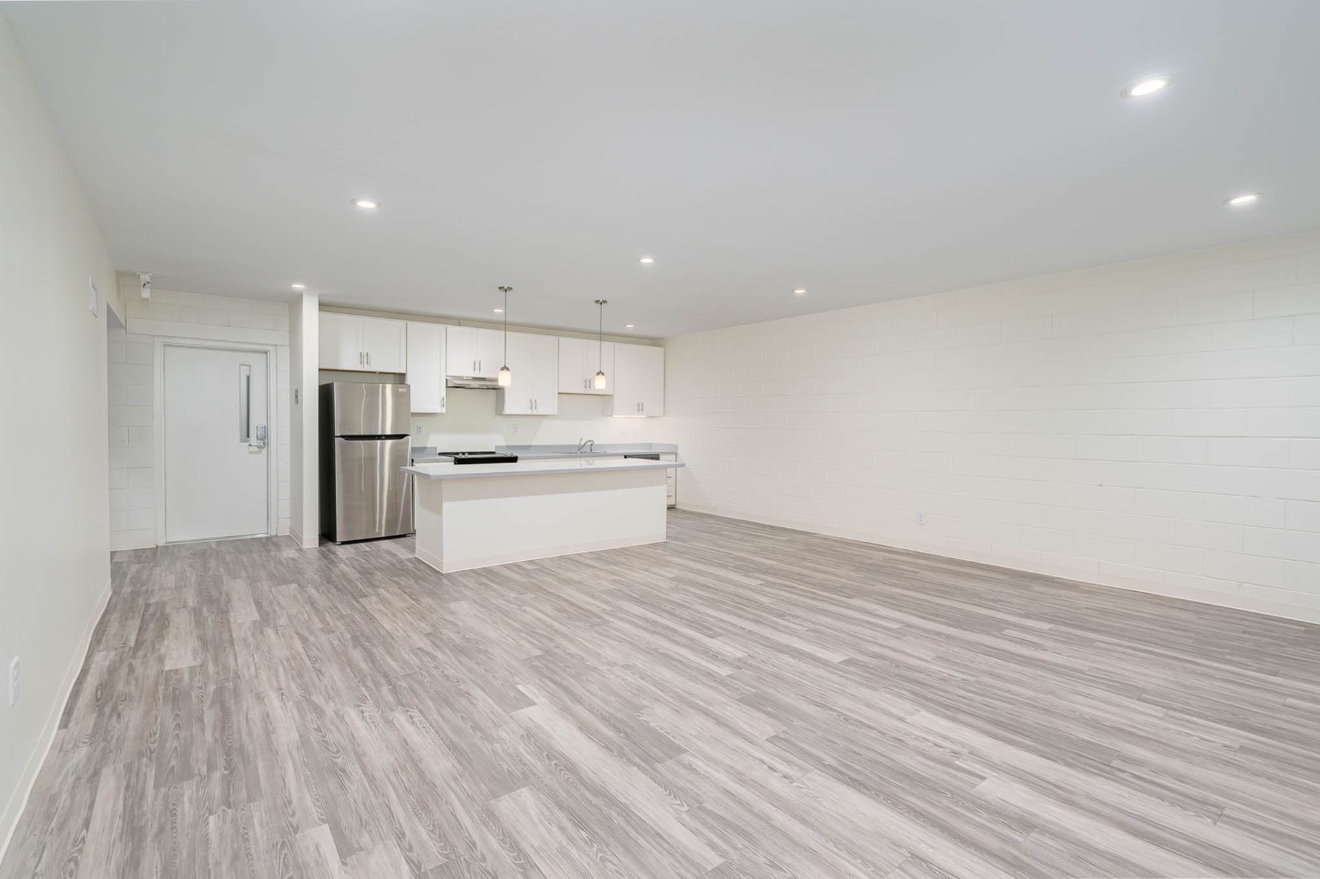 An empty living room with hardwood floors and a kitchen in the background.
