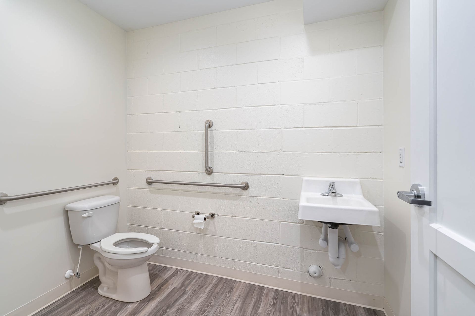 A bathroom with a toilet , sink and handrails.