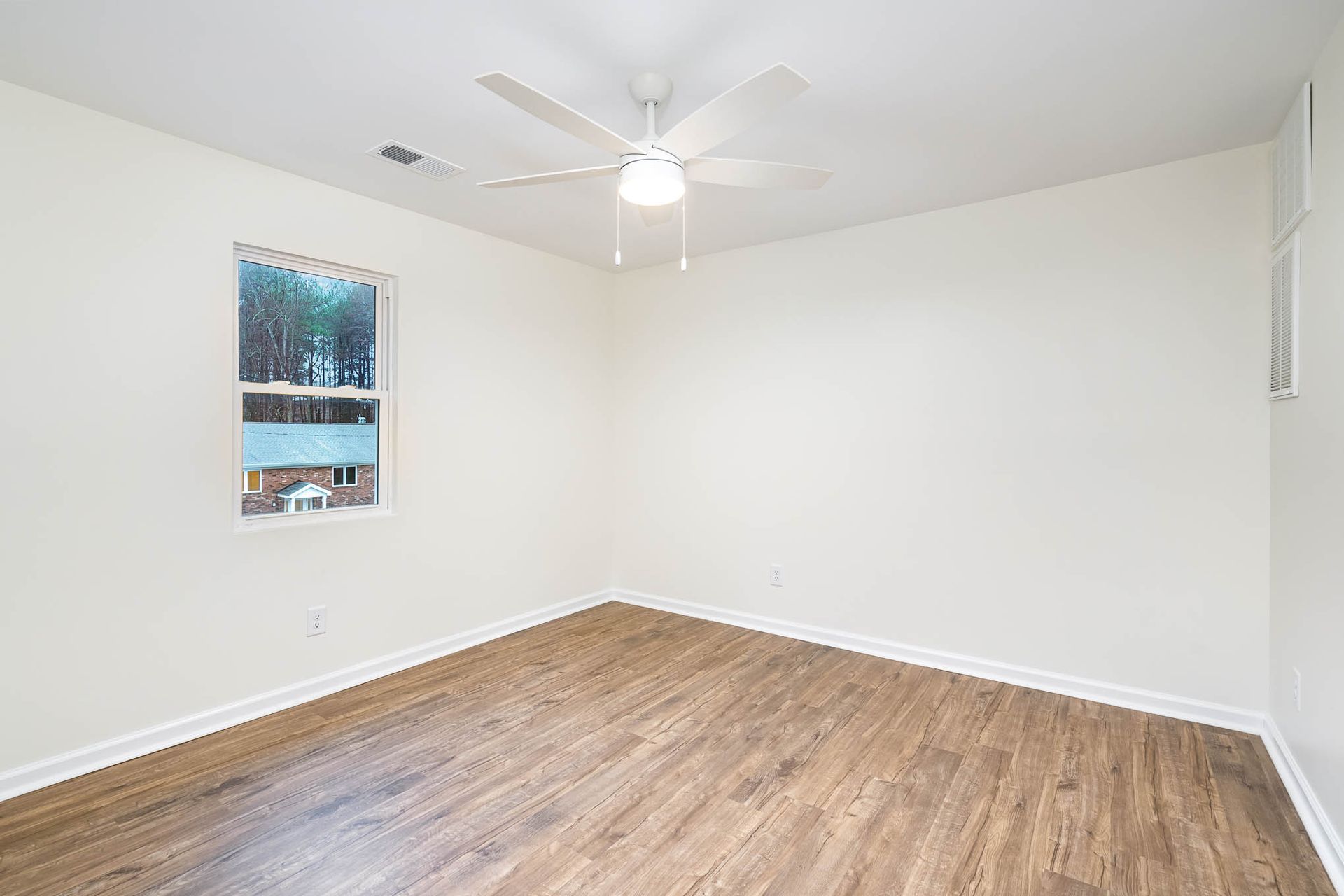 An empty bedroom with hardwood floors and a ceiling fan.