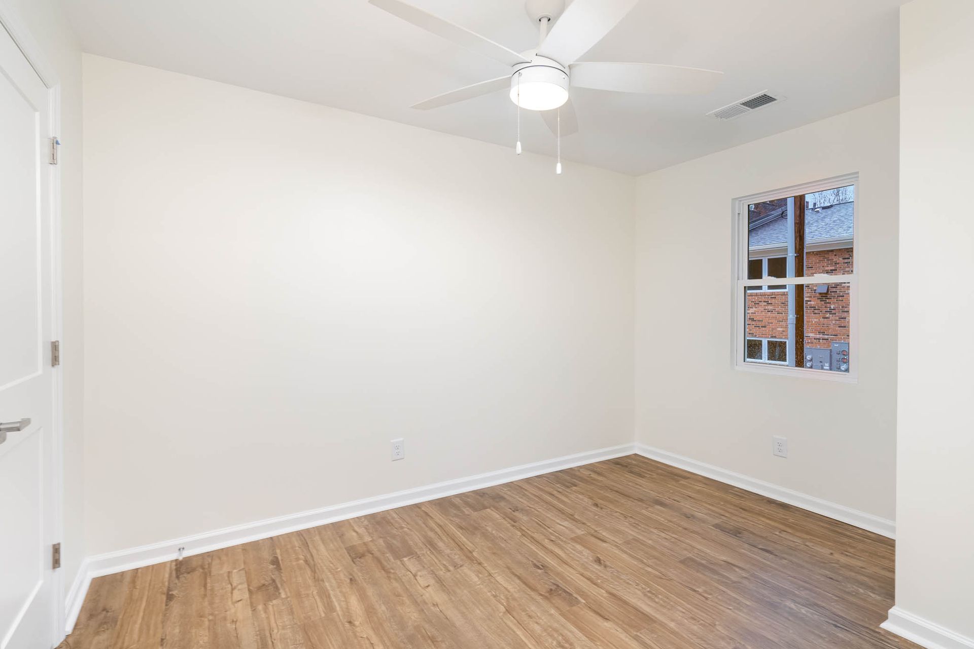 An empty bedroom with hardwood floors and a ceiling fan.