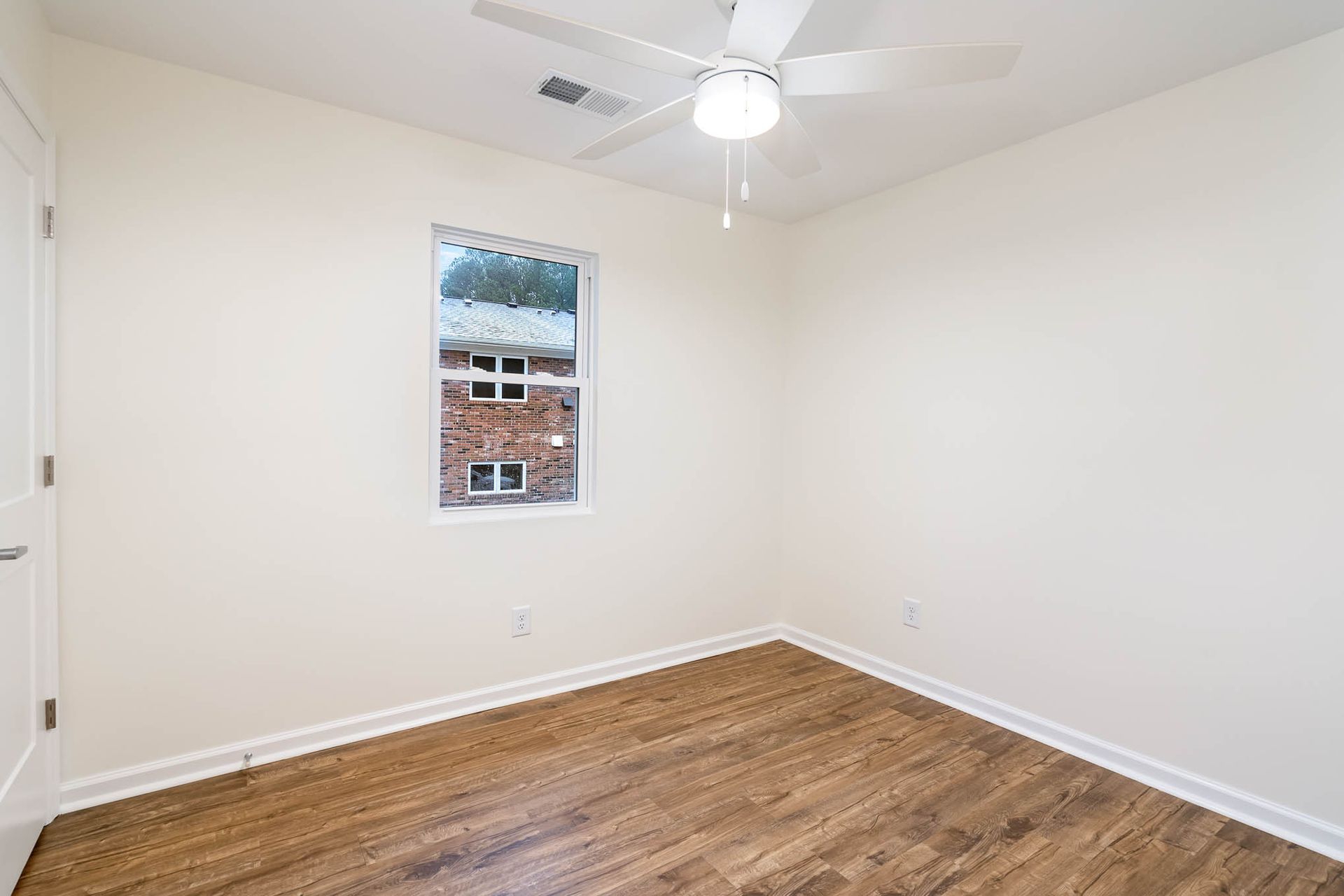 An empty bedroom with hardwood floors and a ceiling fan.