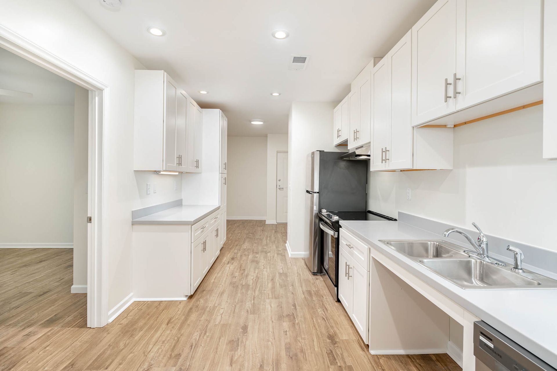 A kitchen with white cabinets , a black refrigerator , a sink , and a dishwasher.