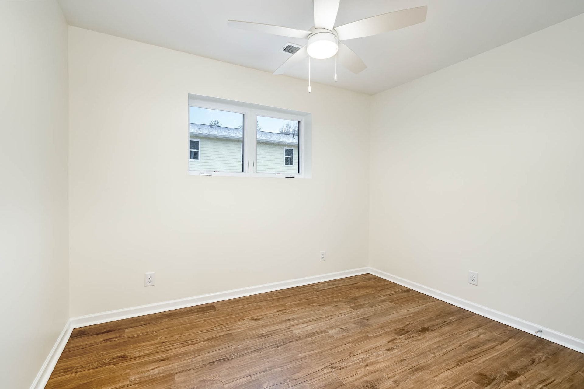 An empty bedroom with hardwood floors and a ceiling fan.