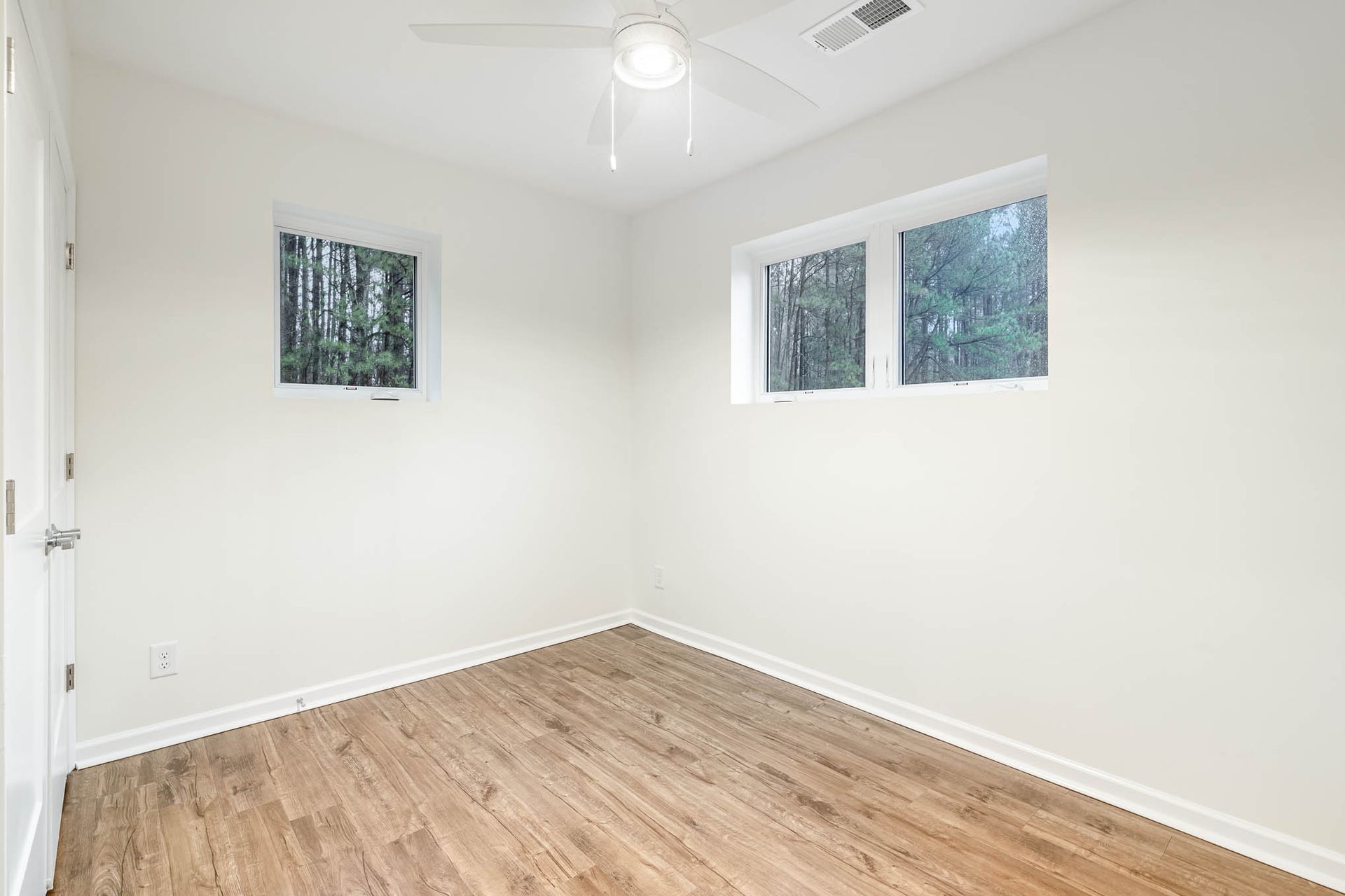 An empty bedroom with hardwood floors , white walls and a ceiling fan.