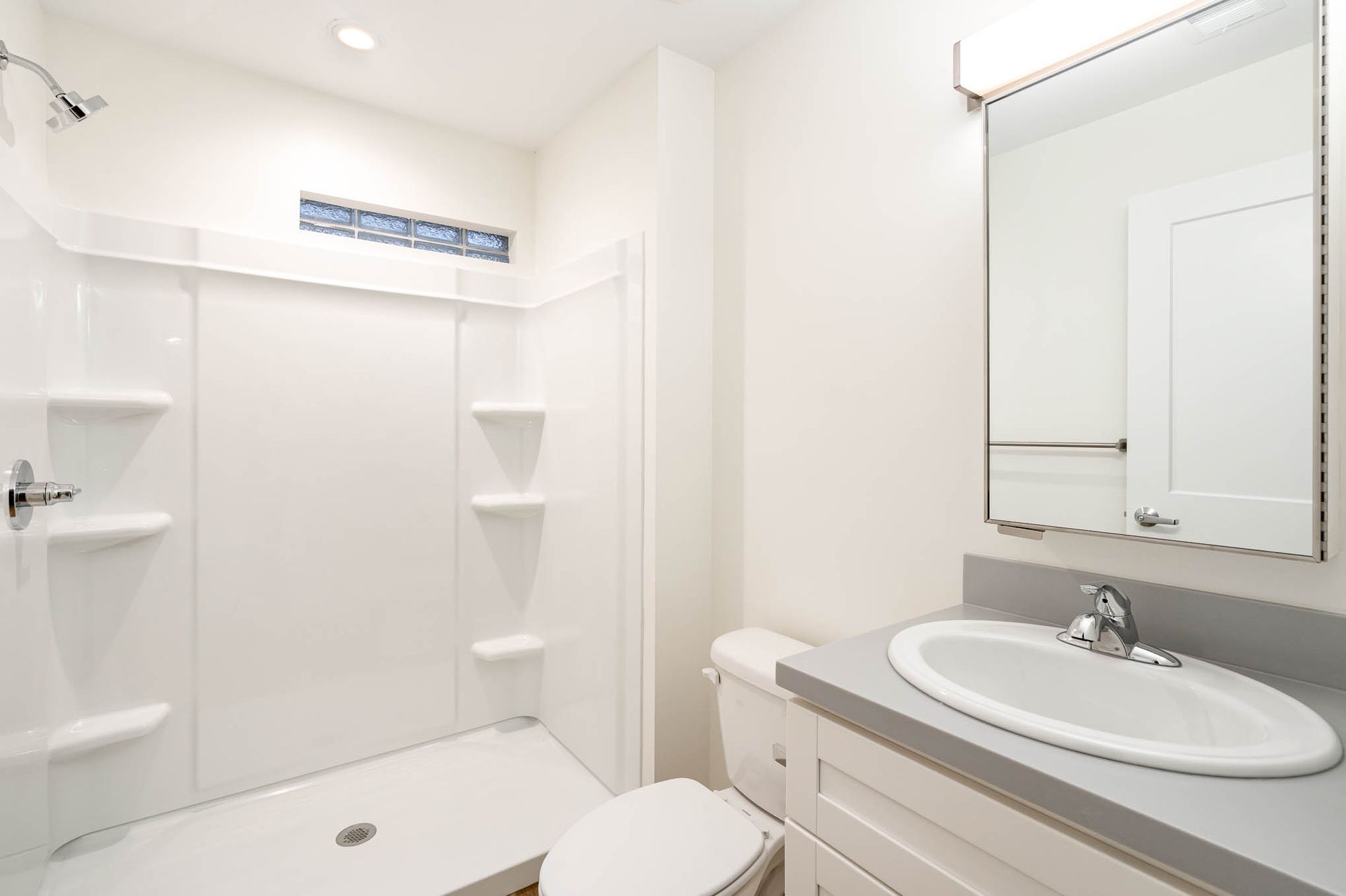 A bathroom with a toilet , sink , shower and mirror.