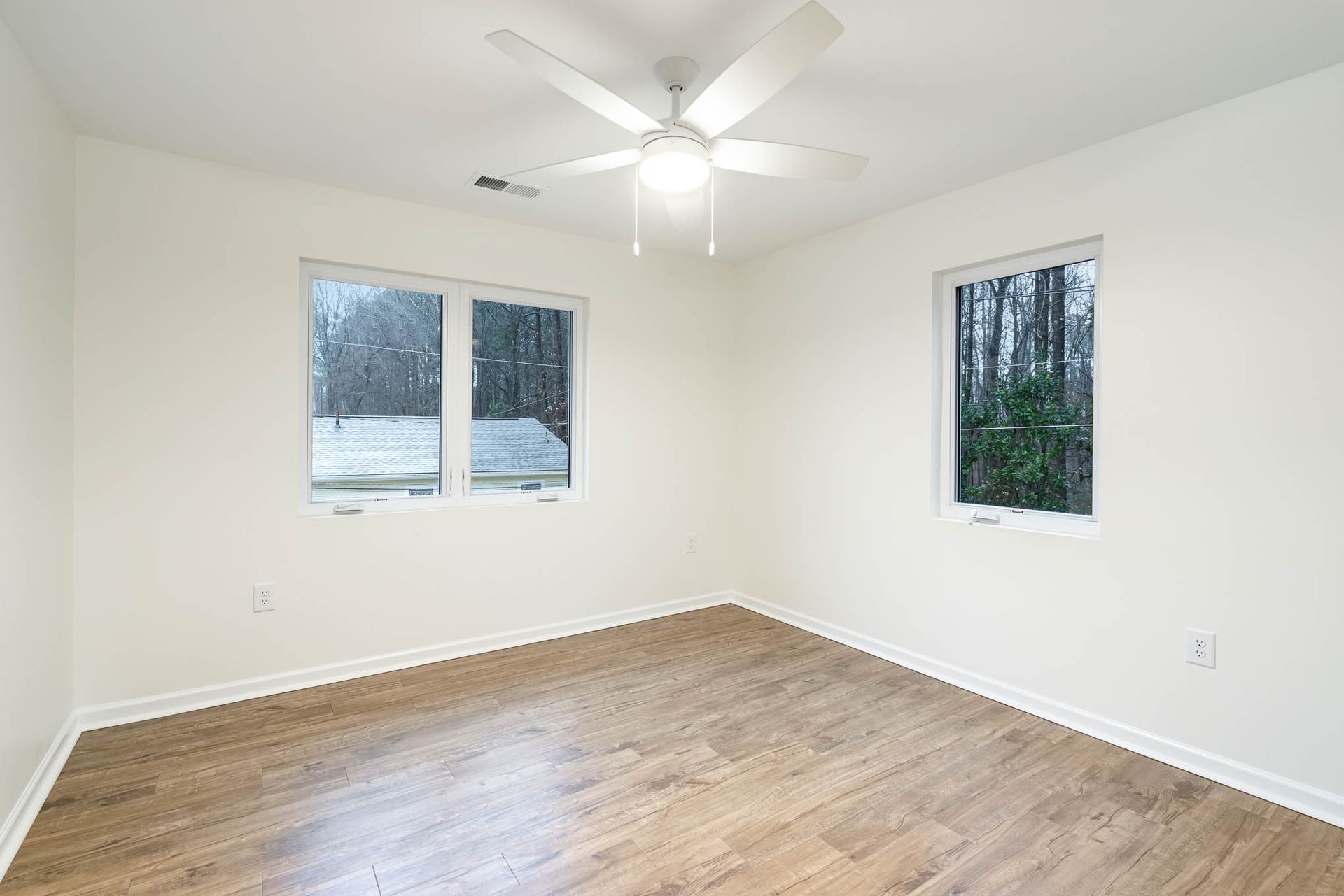 An empty bedroom with hardwood floors and a ceiling fan.