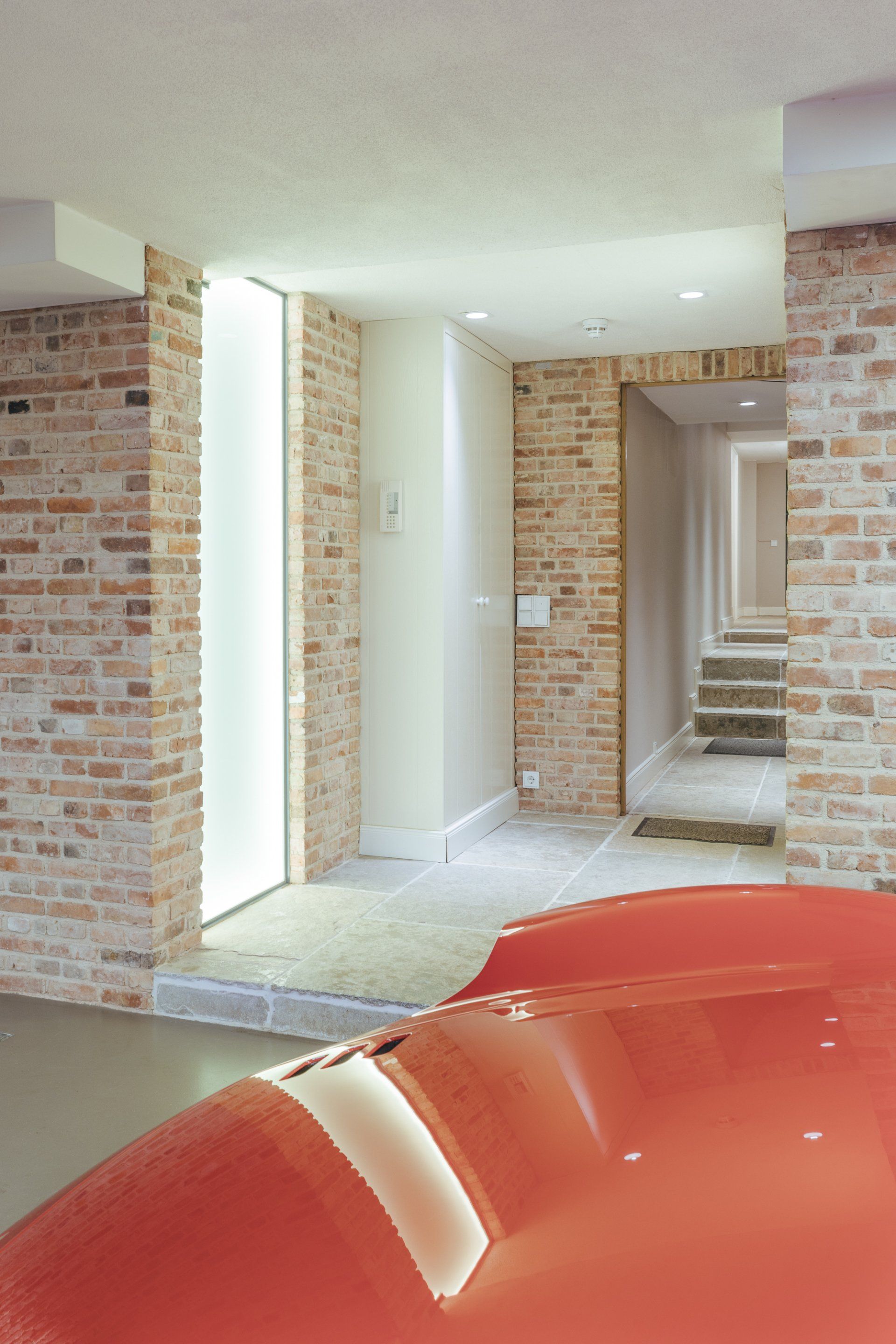 Ein langer Flur mit Backsteinmauern und einem roten Stuhl im Vordergrund