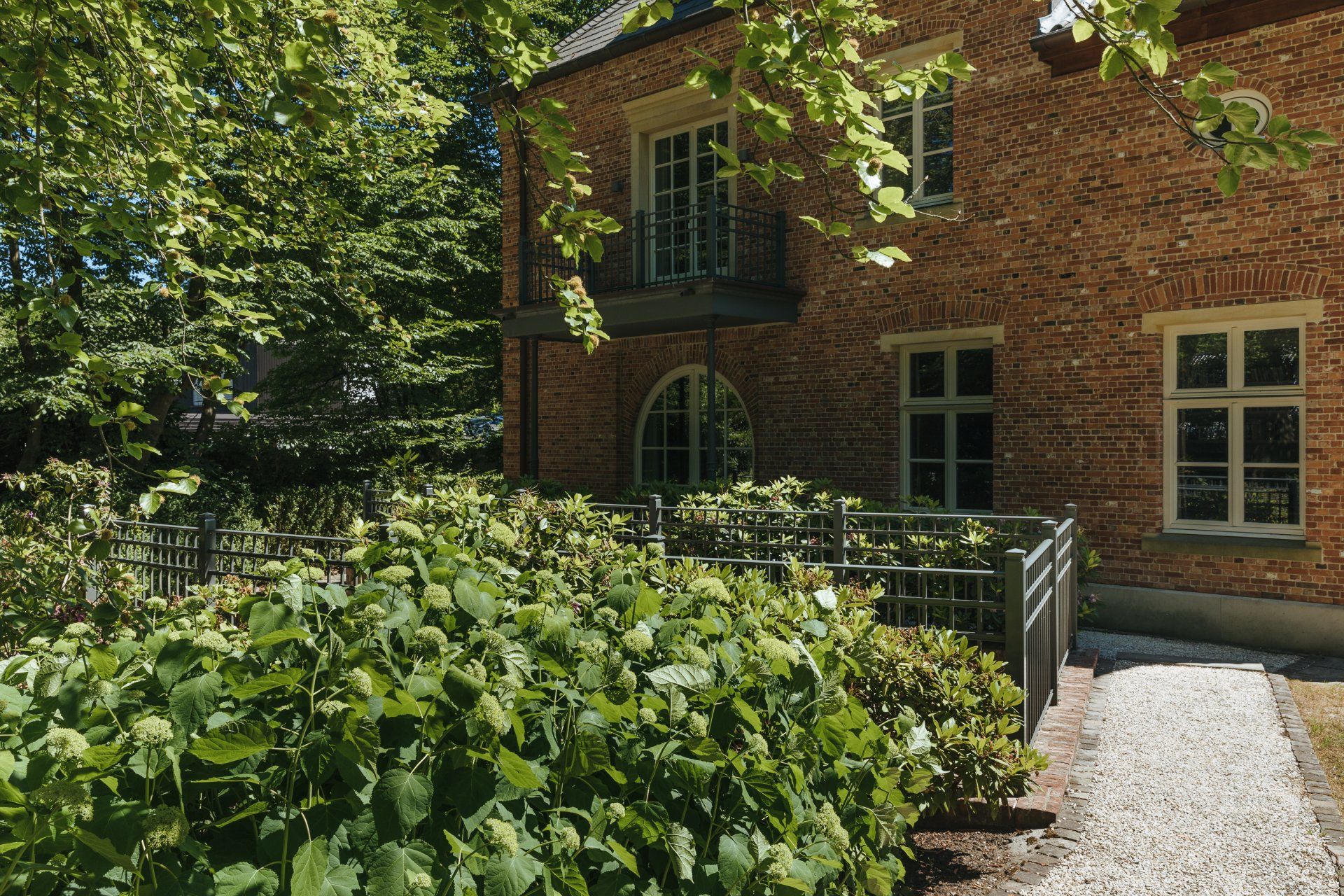 Ein Backsteingebäude mit einem dorthin führenden Gehweg, umgeben von Bäumen und Büschen.