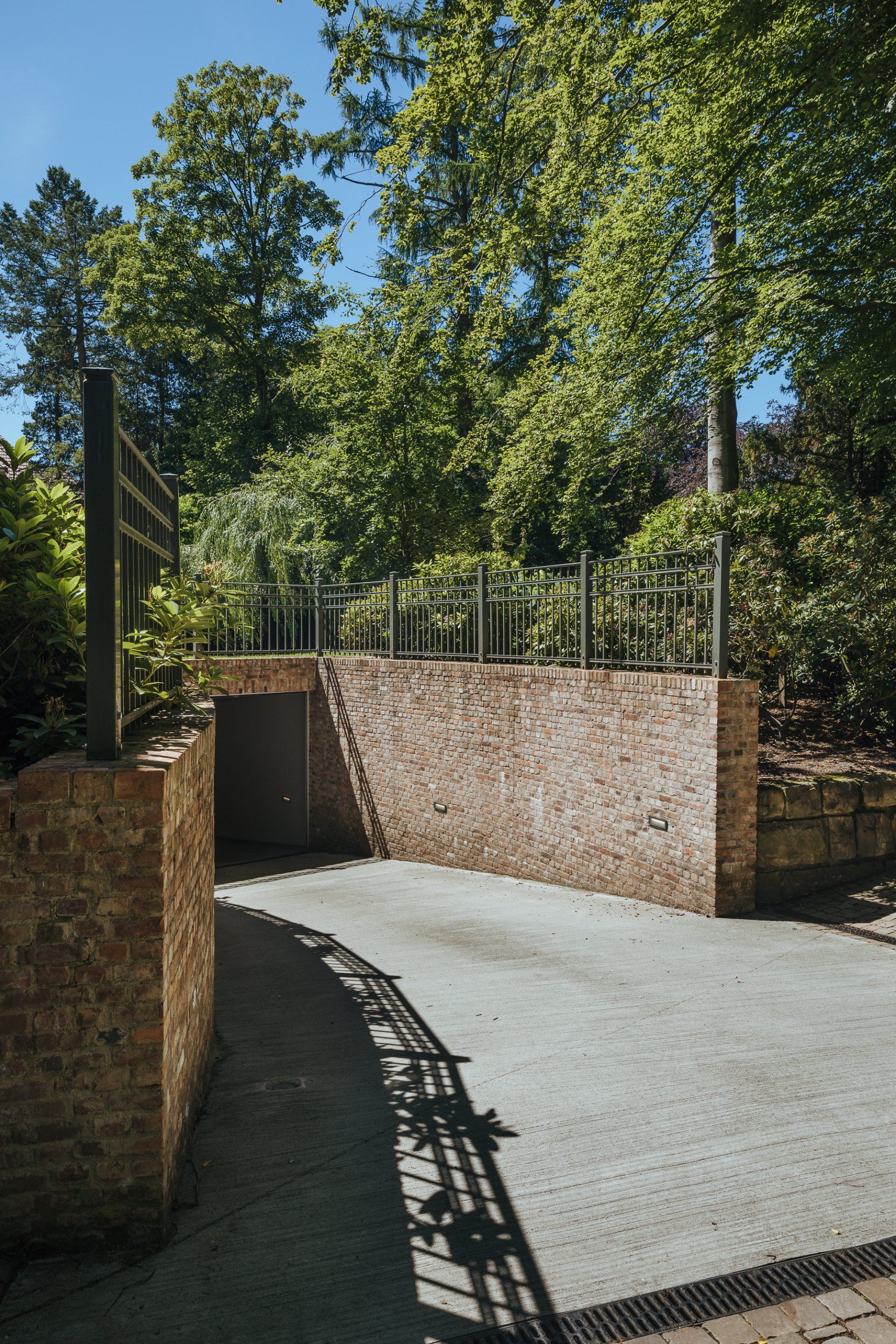Eine Backsteinmauer umgibt eine Einfahrt, im Hintergrund sind Bäume zu sehen.
