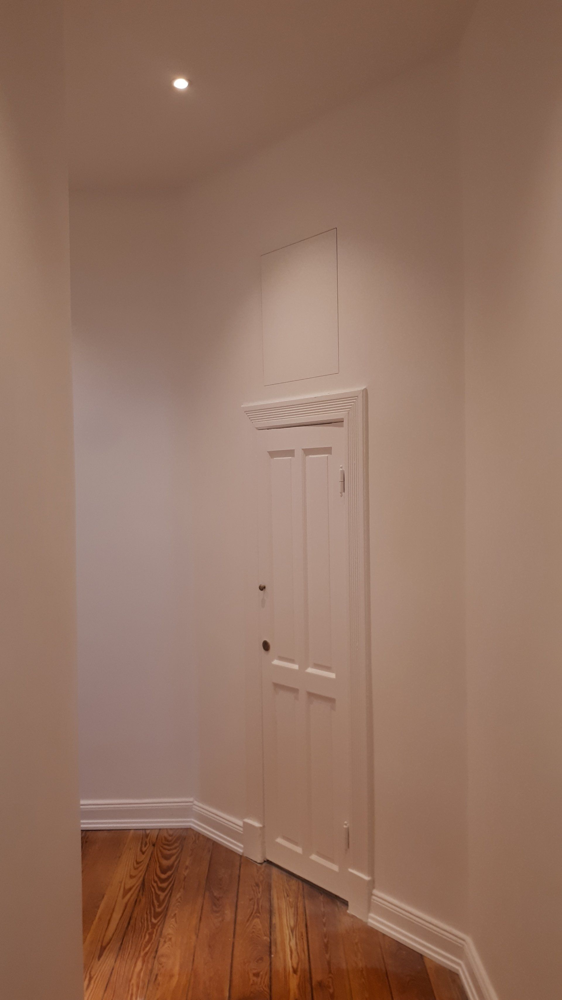 Ein Flur mit weißer Tür und Holzboden.