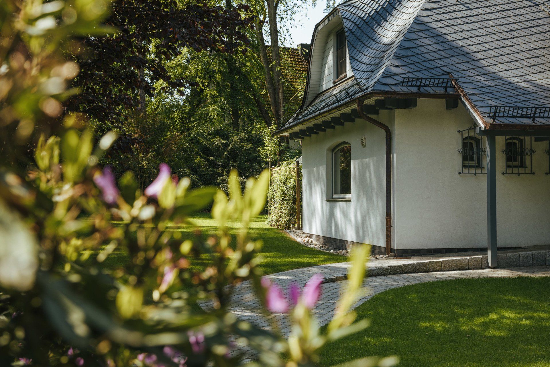 Ein weißes Haus mit blauem Dach ist von Bäumen und Blumen umgeben.