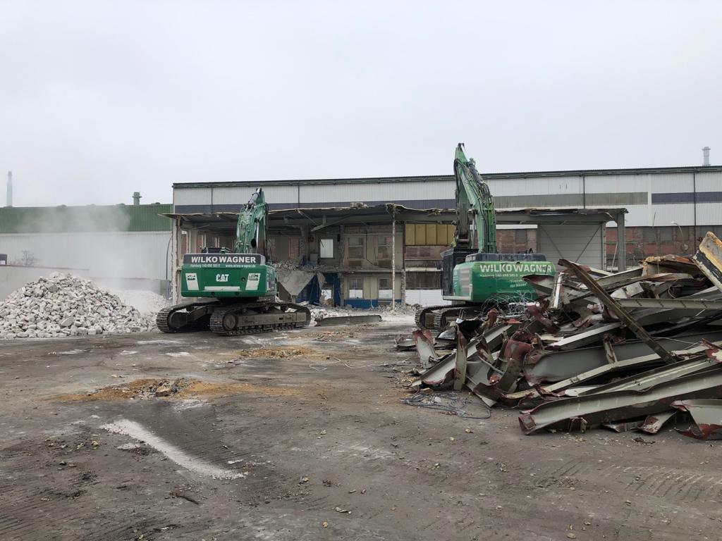 Zwei grüne Bagger zerstören auf einem Feld ein Gebäude.