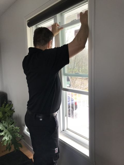 Un homme en chemise noire se tient devant une fenêtre.