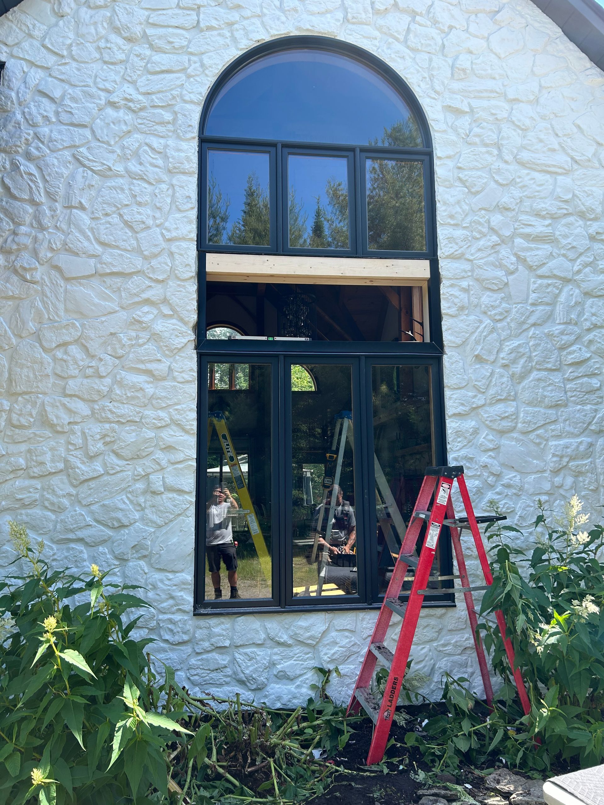 Une échelle est posée devant une grande fenêtre sur un bâtiment blanc.