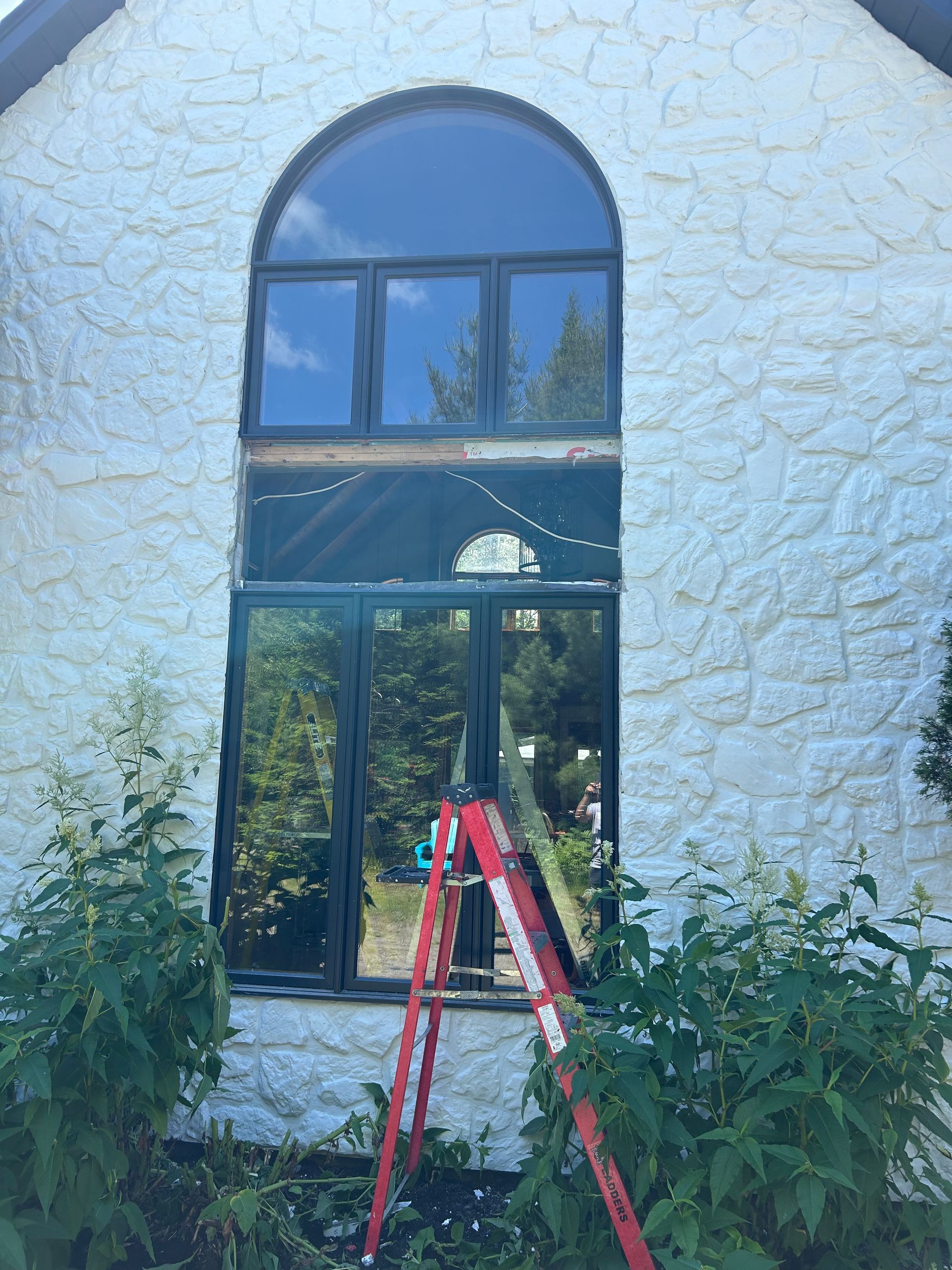 Une échelle est posée devant une grande fenêtre sur un bâtiment blanc.