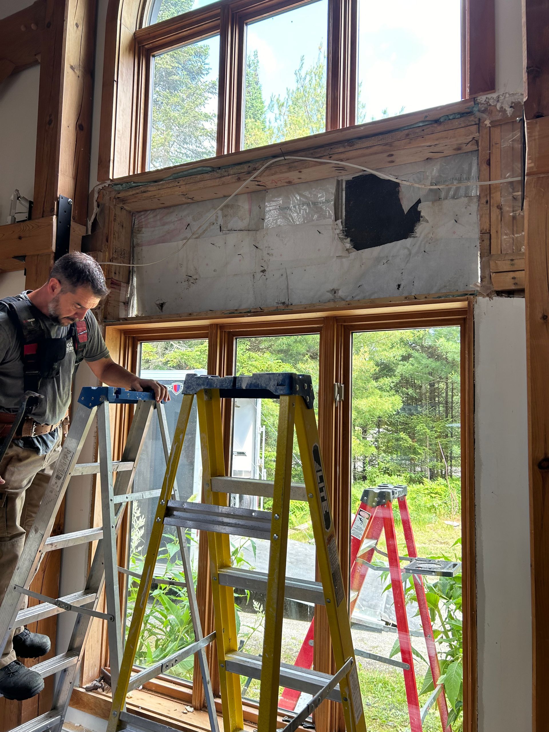 Un homme est debout sur une échelle devant une fenêtre.