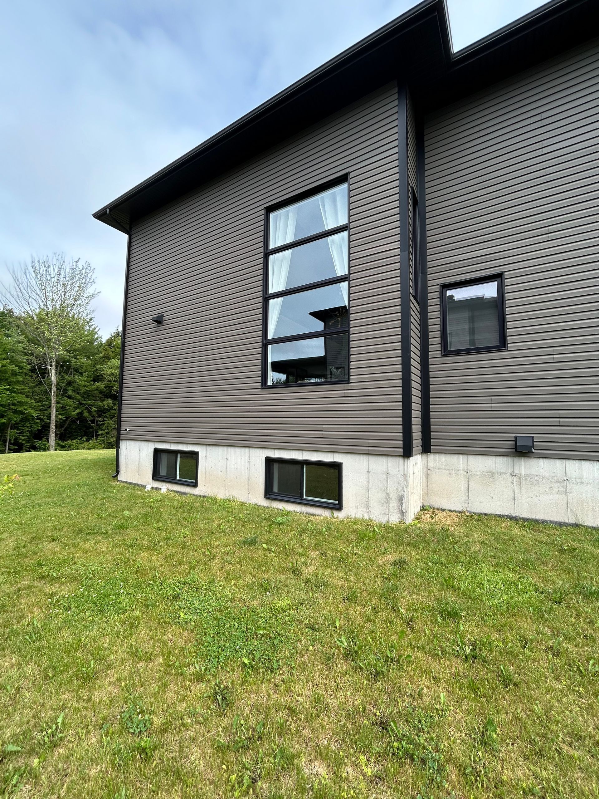 Une grande maison avec beaucoup de fenêtres est située au sommet d'un champ vert luxuriant.