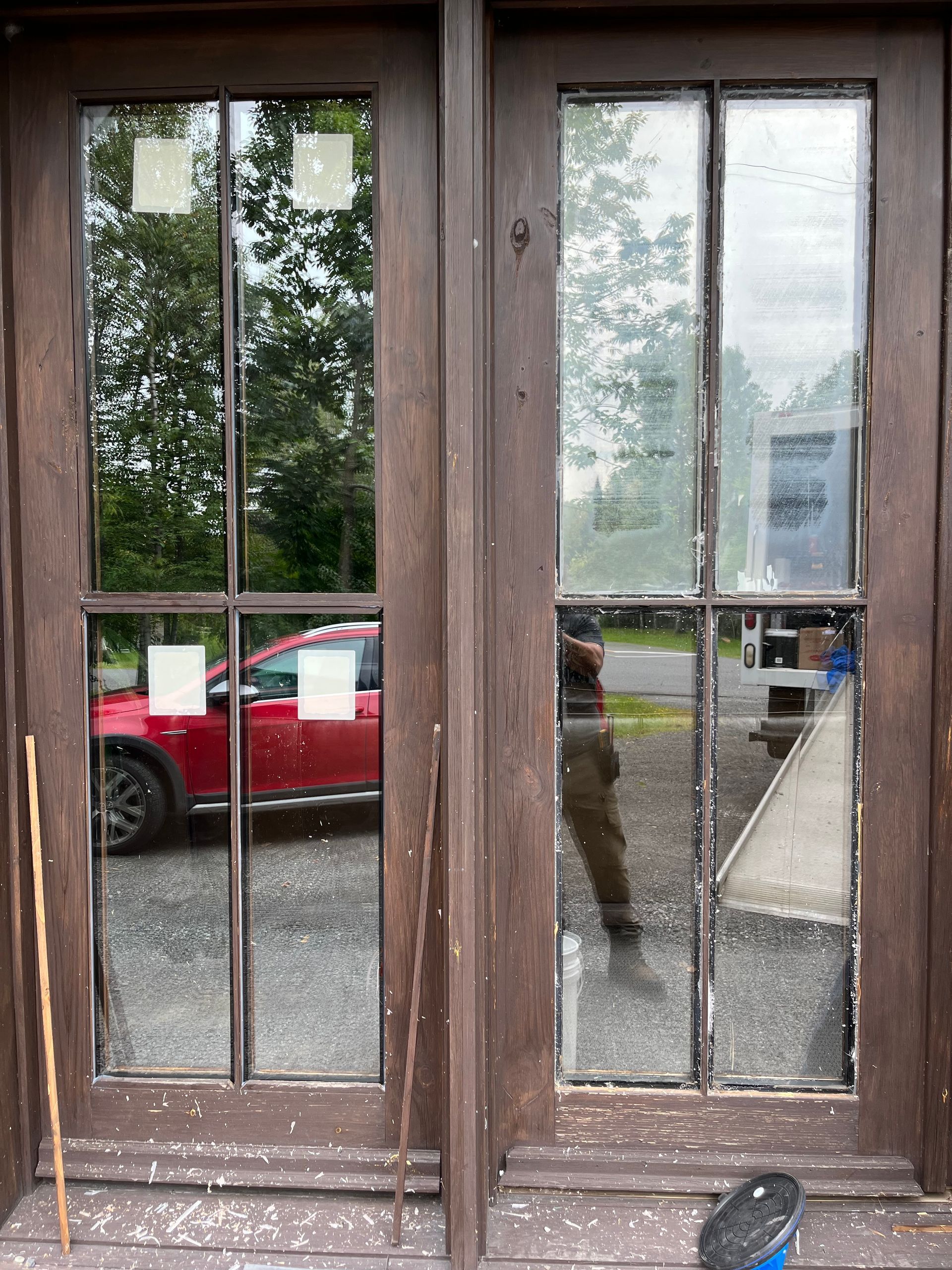 Une voiture rouge se reflète dans les vitres d'une porte en bois.