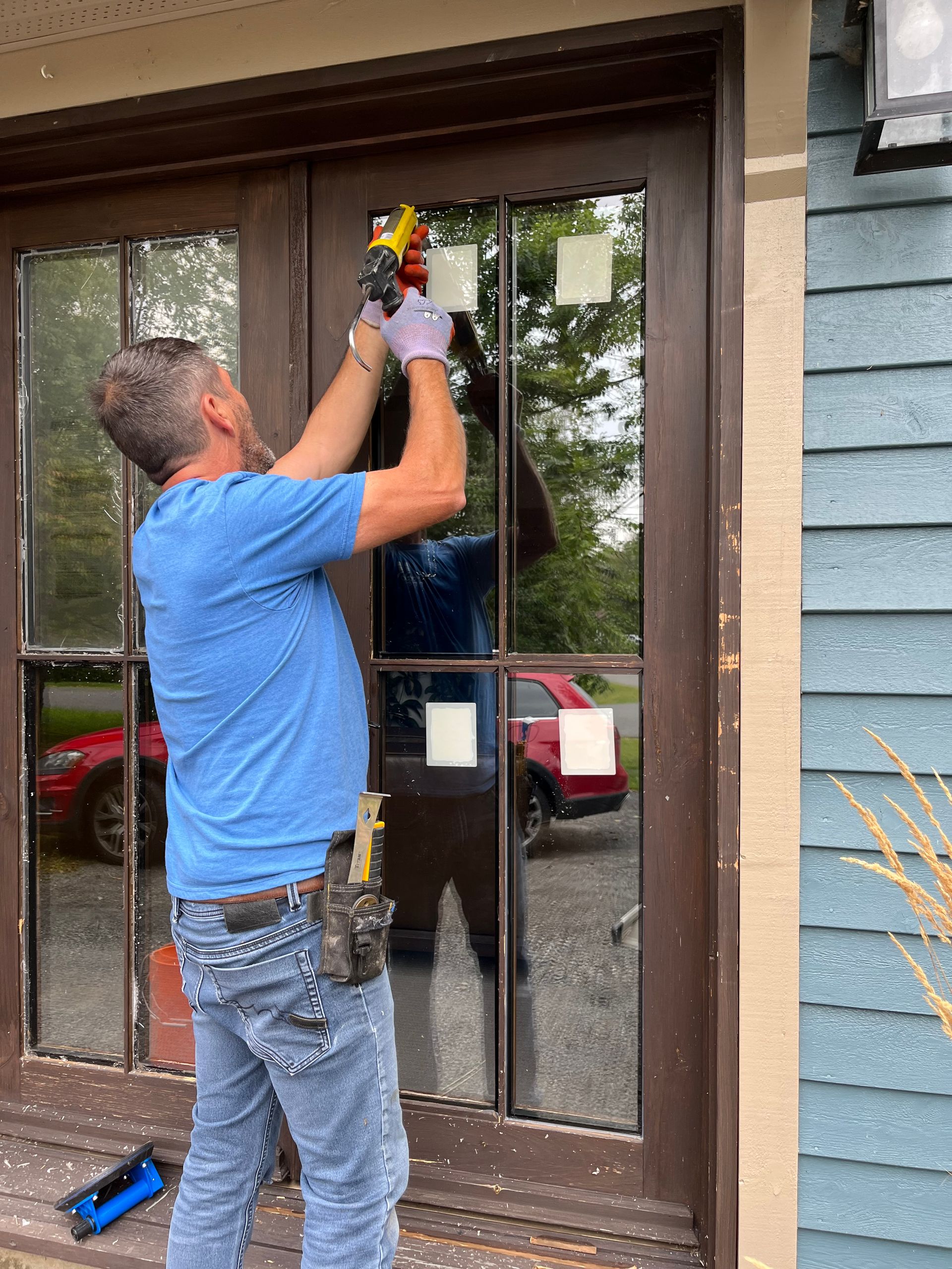 Un homme installe une porte vitrée sur une maison.