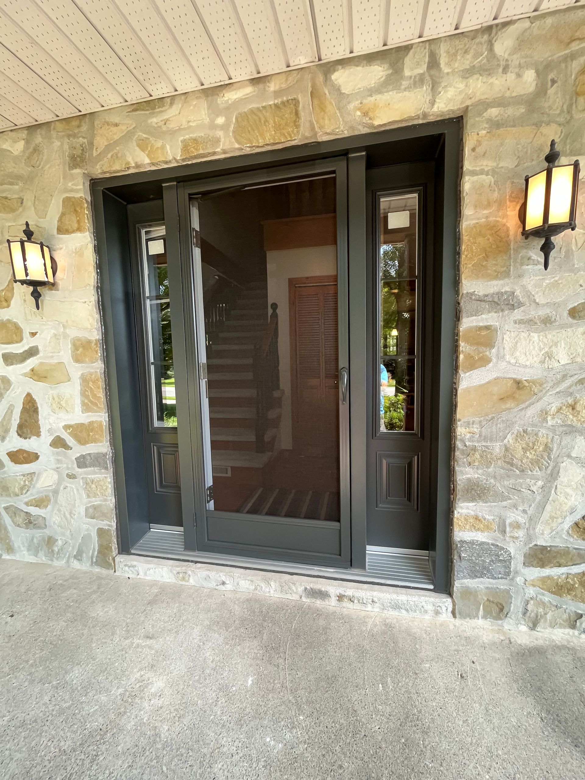 Un mur de pierre avec une porte noire et un escalier en arrière-plan.