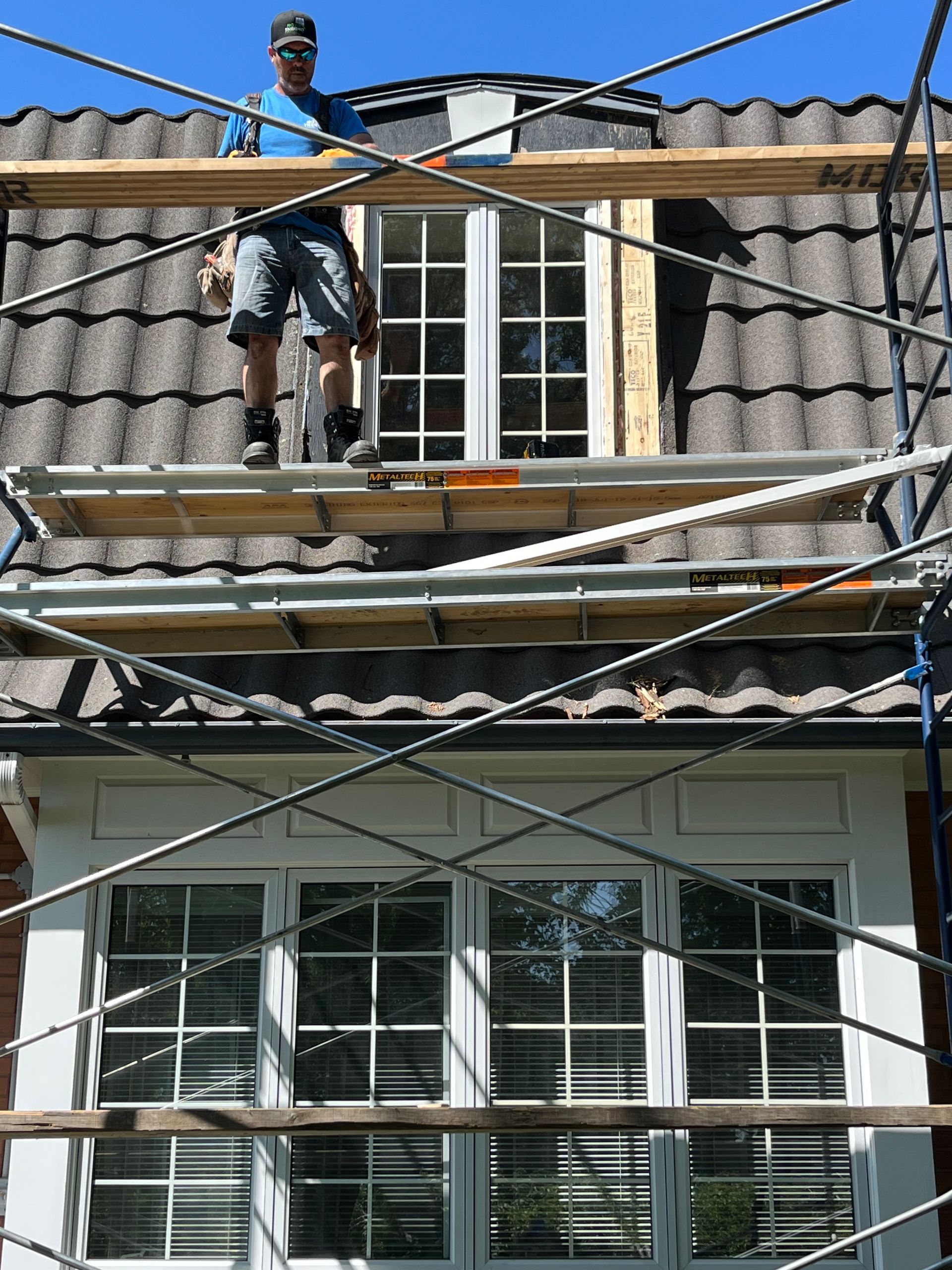 Un homme est debout sur un échafaudage sur le toit d'une maison.