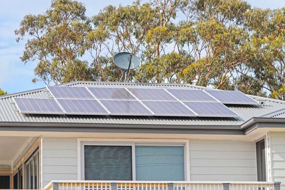 A Row of Solar Panels on a Gray Corrugated Metal Roof Above a House — Brian Williams Electrical Air Solar in Cooroibah, QLD