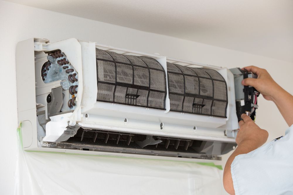 Person Cleaning a Wall-mounted Air Conditioner — Brian Williams Electrical Air Solar in Caloundra, QLD