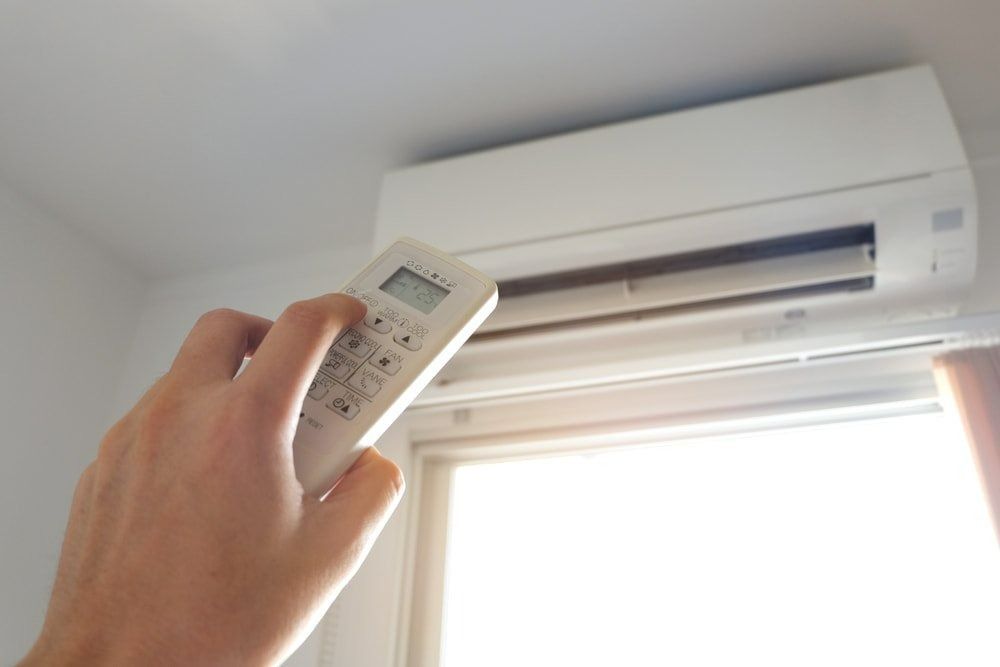 Hand Pointing Remote Control at a White Air Conditioner — Brian Williams Electrical Air Solar in Cooroibah, QLD