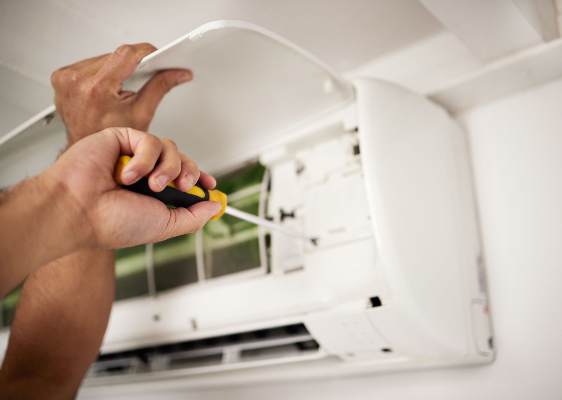 Person using a screwdriver to open a white wall-mounted air conditioning unit.