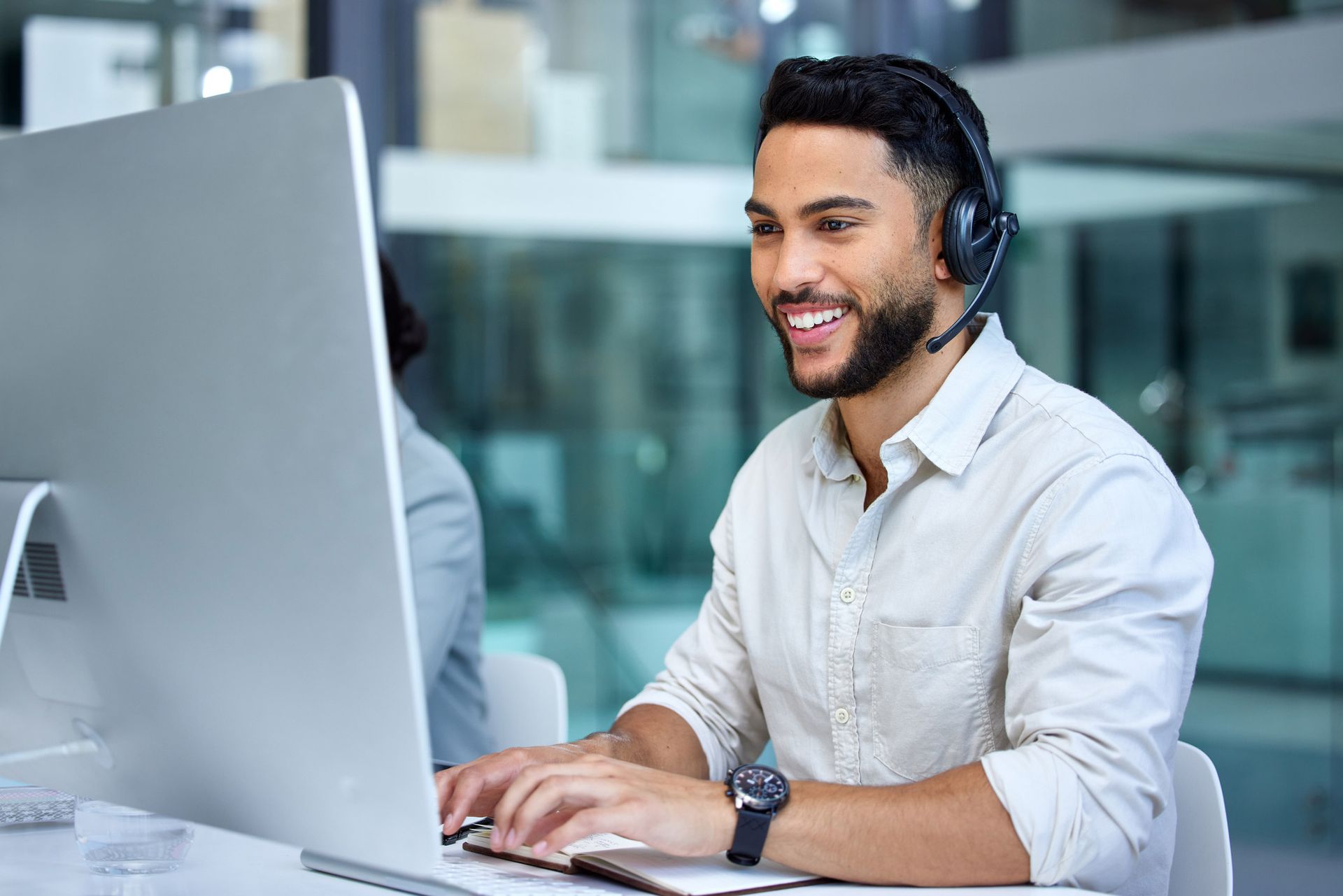 Man wearing headset, typing at computer, smiling in office.