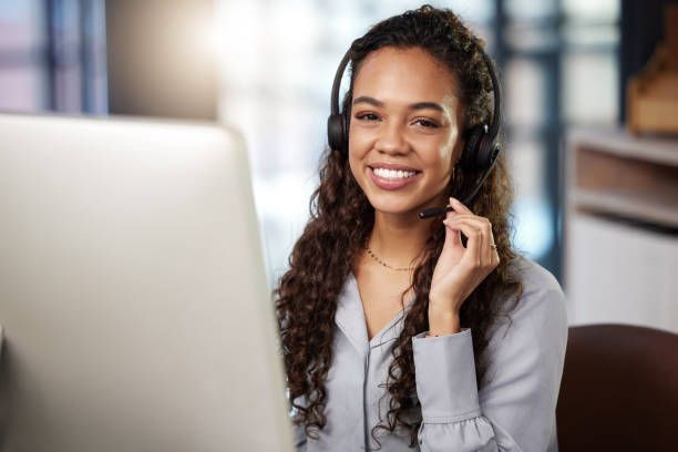 Woman with curly hair smiles while wearing a headset, in front of a computer.