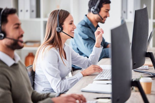 Three people with headsets working at computers in an office.