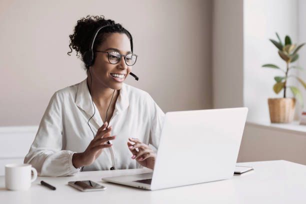 Woman with headset on a video call at a desk with a laptop, smiling.