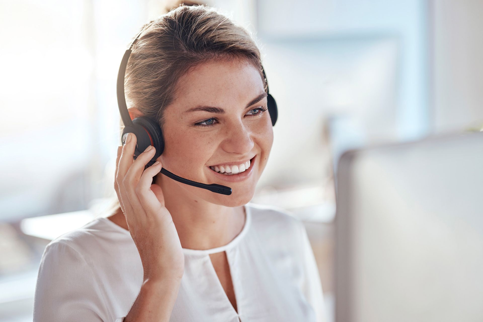 Woman wearing a headset smiles while looking at a computer screen in an office.