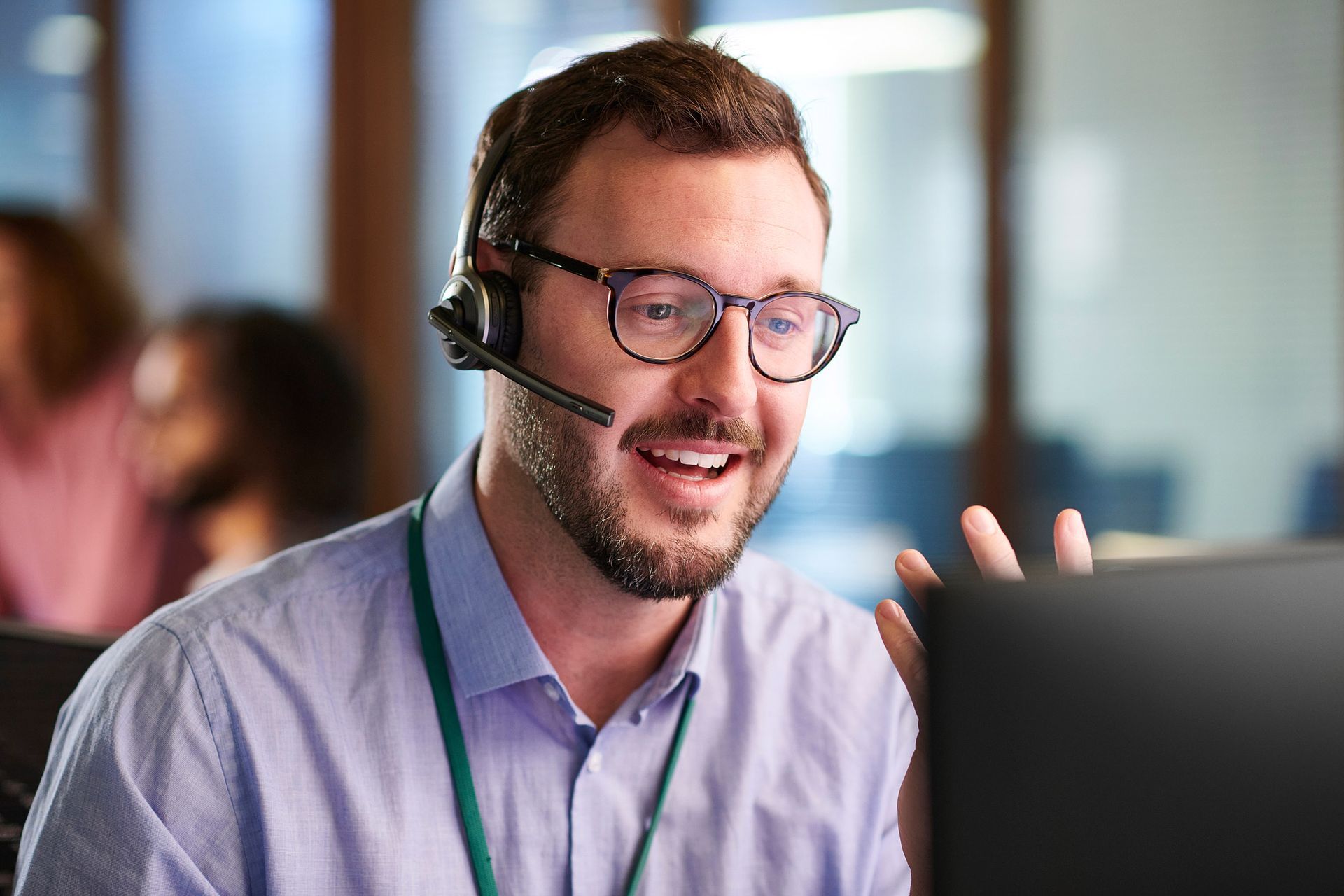 Man with glasses and headset smiles while looking at a computer screen in an office.