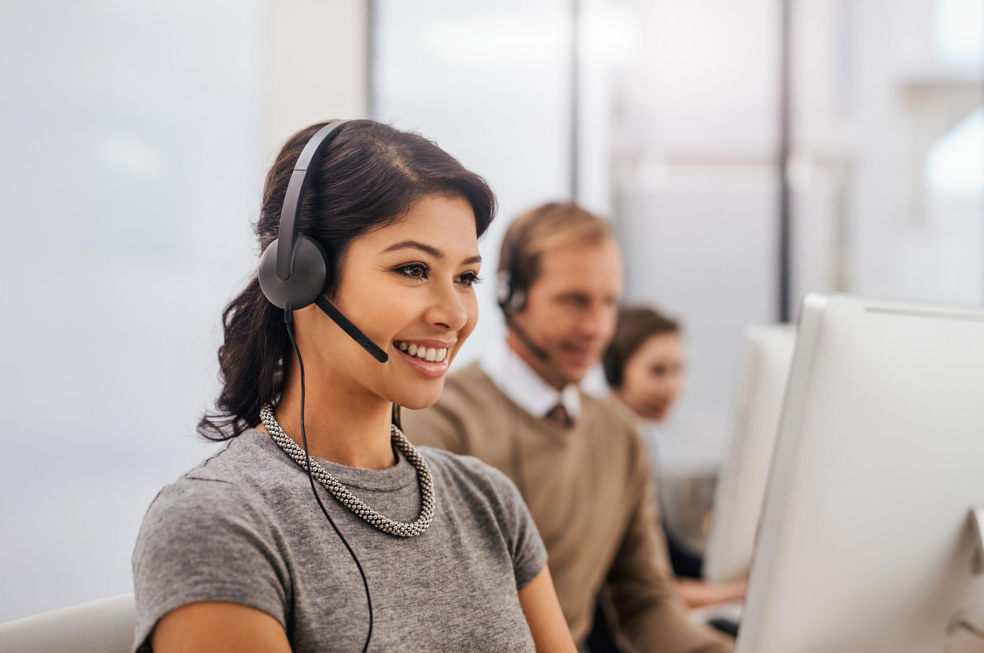 Woman wearing headset, smiling at computer in office with colleagues.