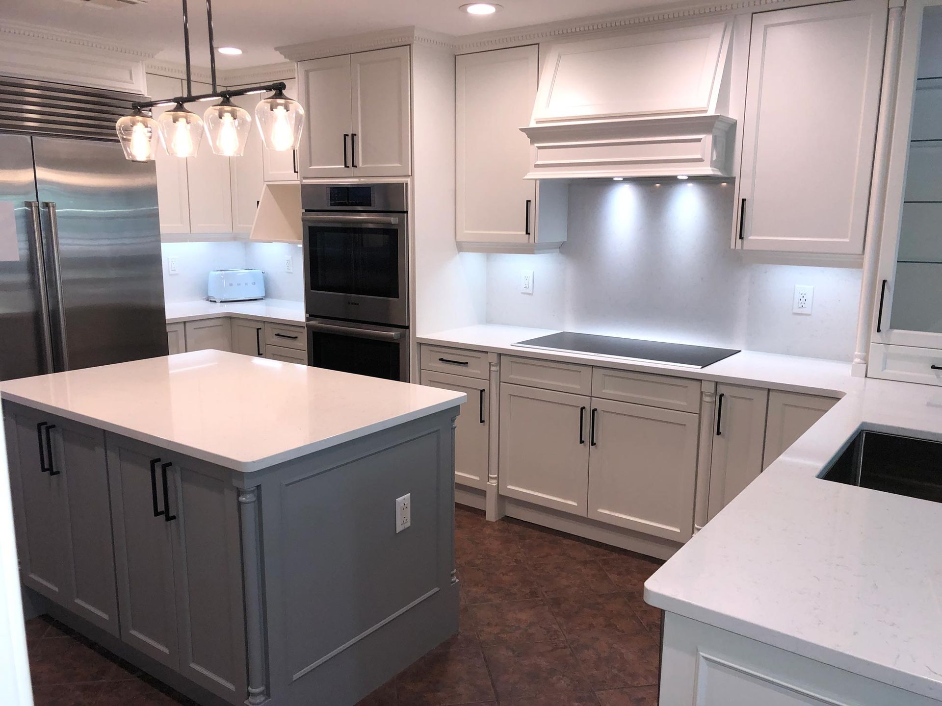 Modern white kitchen with gray island, stainless steel appliances, and overhead lighting.