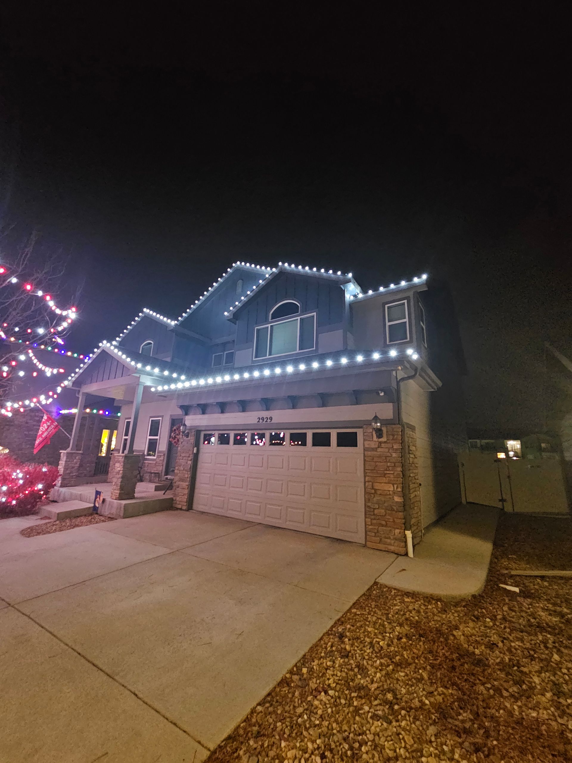 House at night with white Christmas lights along the roofline, and garage.