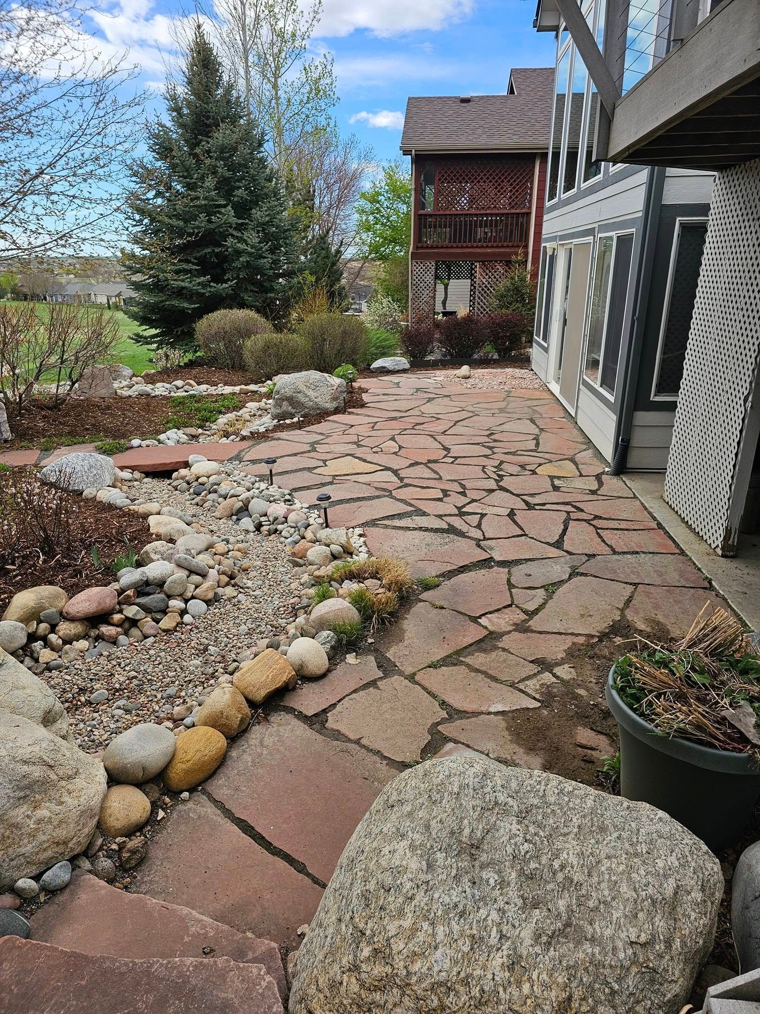 Stone patio and garden with rocks, near a house on a sunny day.