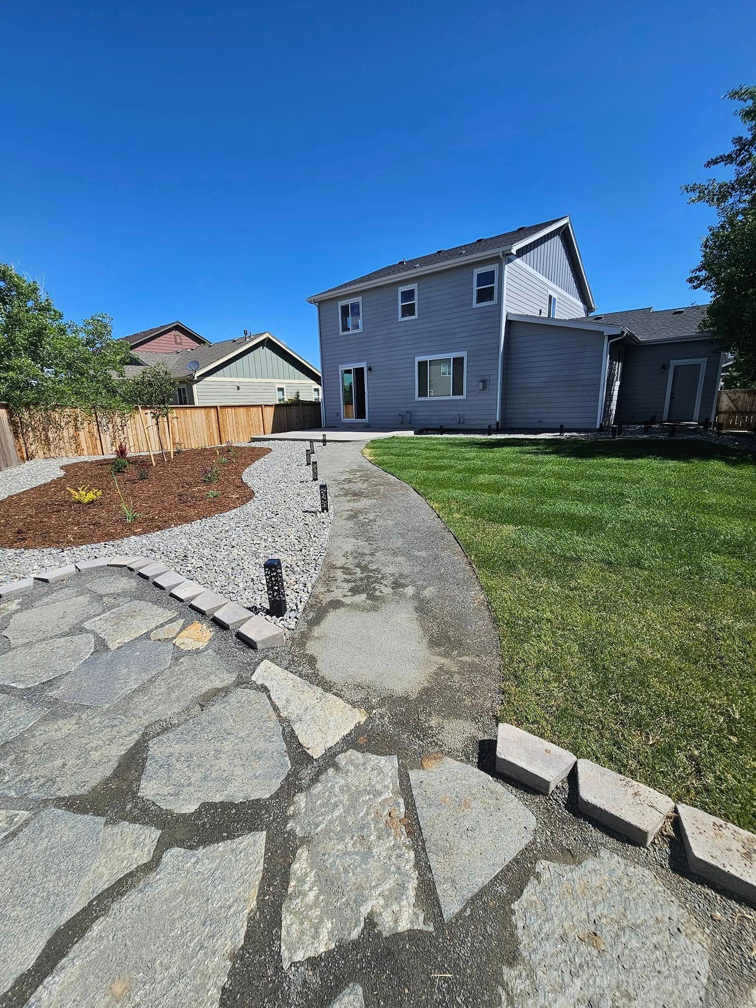 Stone path leads to a two-story gray house under a clear blue sky.
