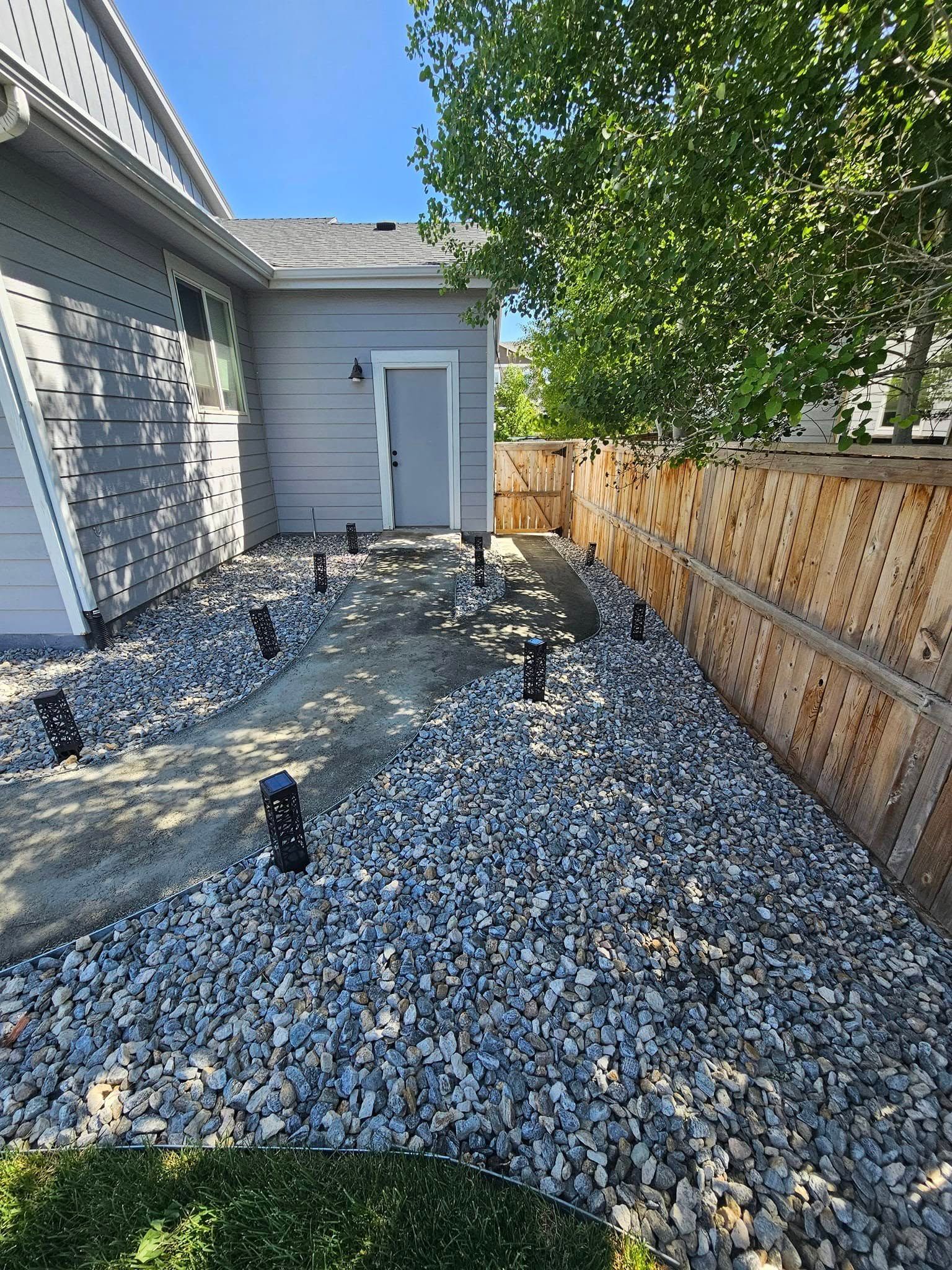 Gravel path with solar lights next to a house and wooden fence.