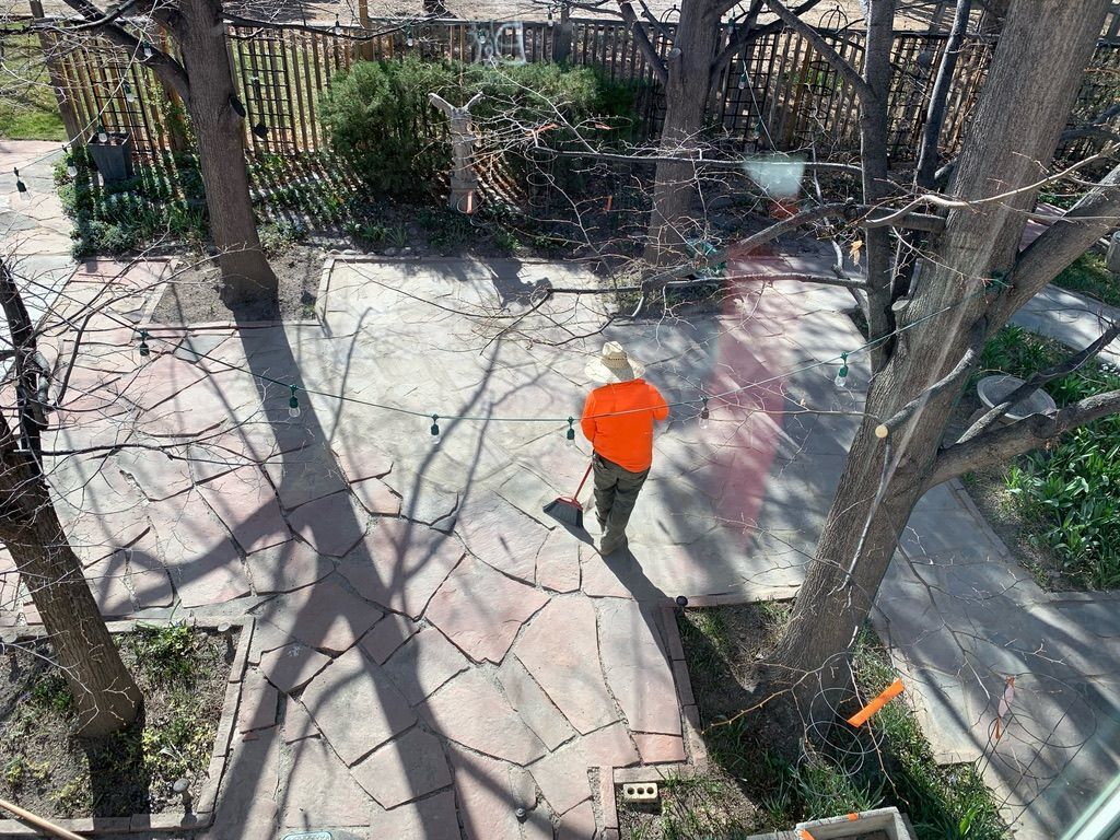 Person in orange shirt walking on a stone patio, shaded by trees.
